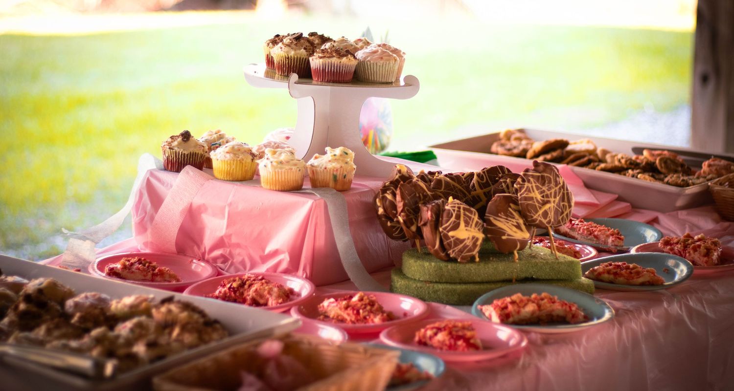 Outdoor dessert table with cupcakes, muffins, and pastries on pink tablecloth at a garden party.