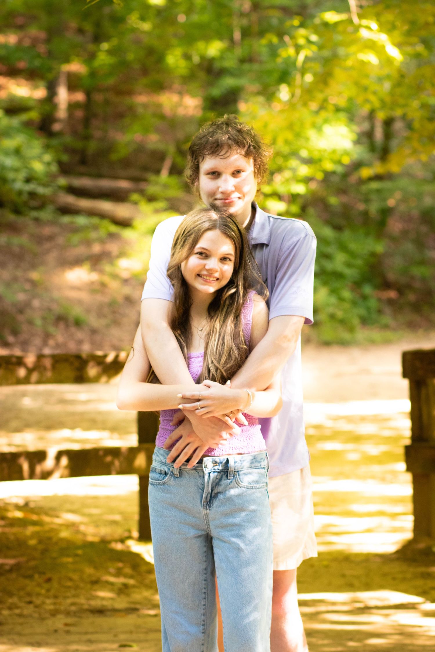 Young couple embracing in a sunny forest park, smiling happily together outdoors.