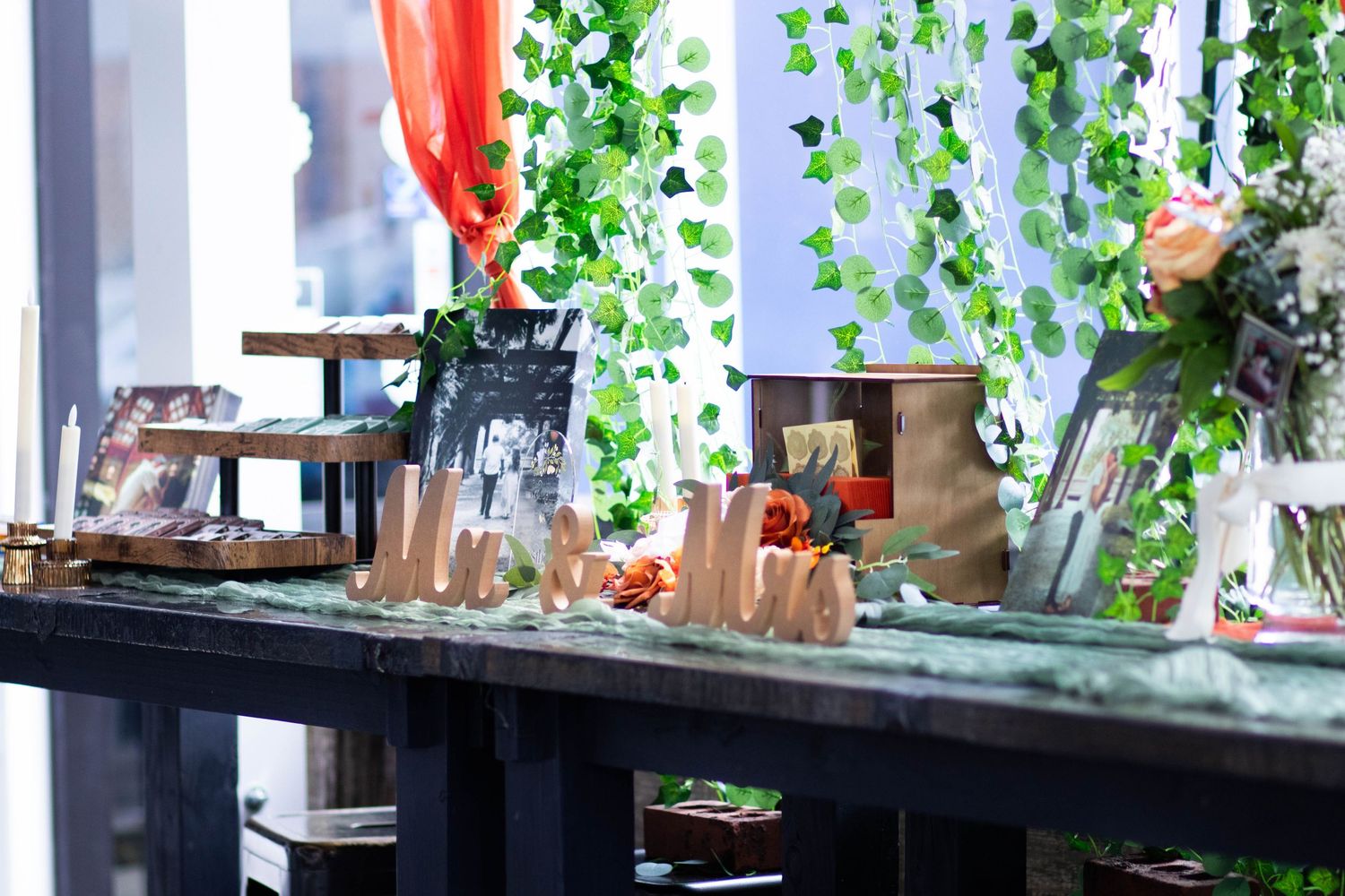 Elegant wedding dessert table decorated with hanging green ivy garlands, wooden signs, and floral arrangements.