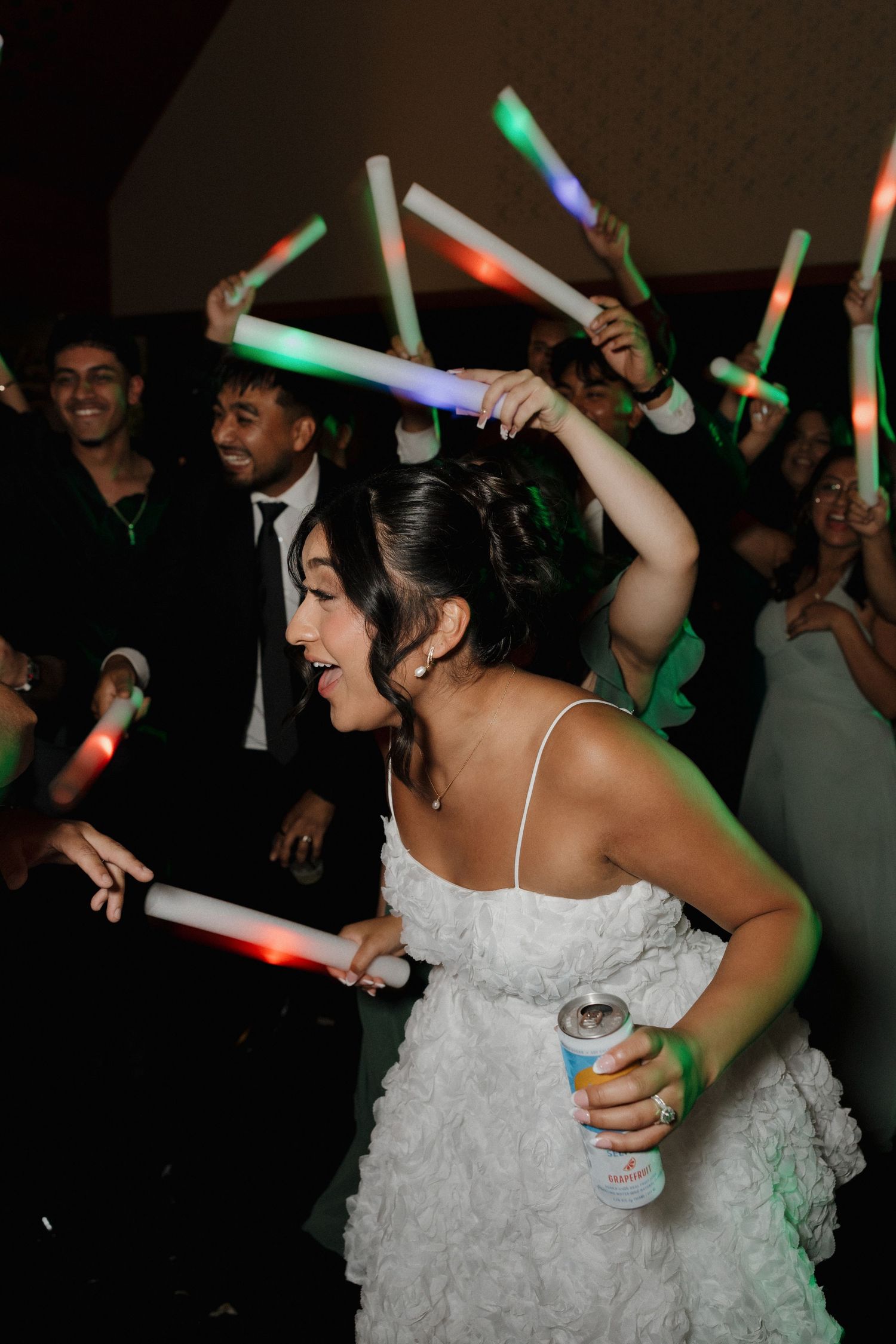 Wedding party guests dance with colorful light-up sticks on a dark dance floor.