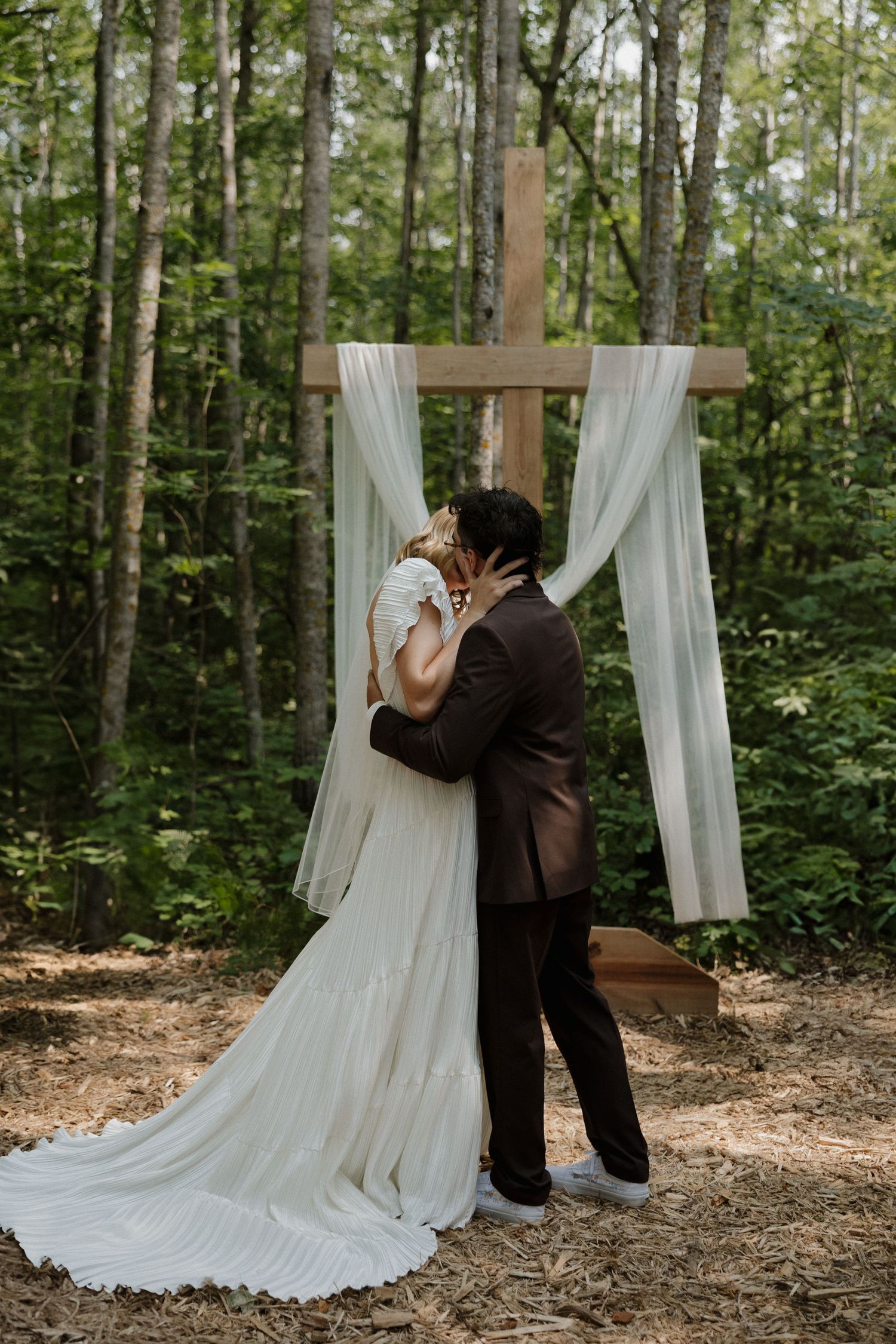 Romantic woodland wedding ceremony with white fabric draped arch and intimate moment.