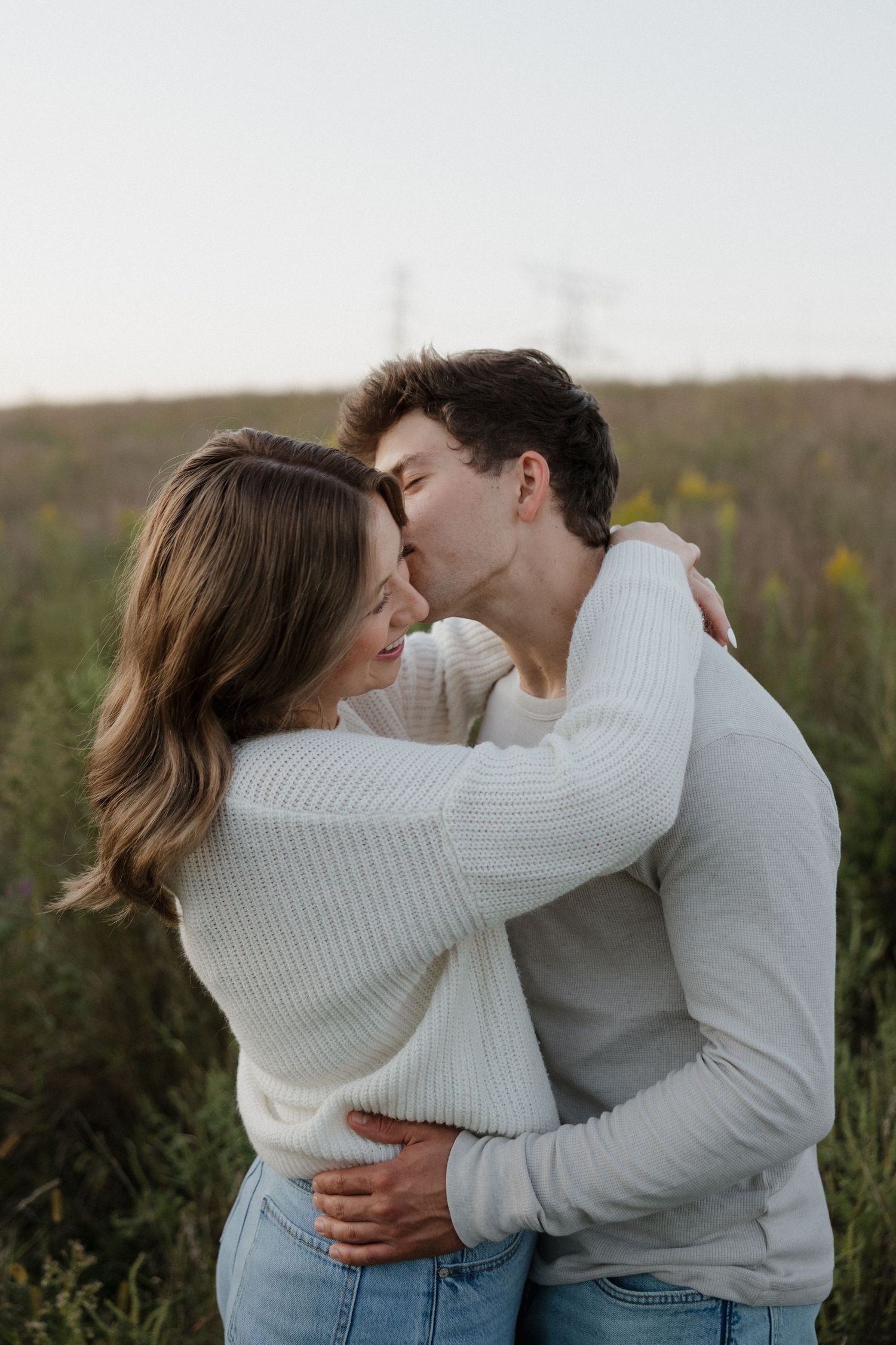 Young couple sharing a tender kiss while embracing in an outdoor field at dusk.