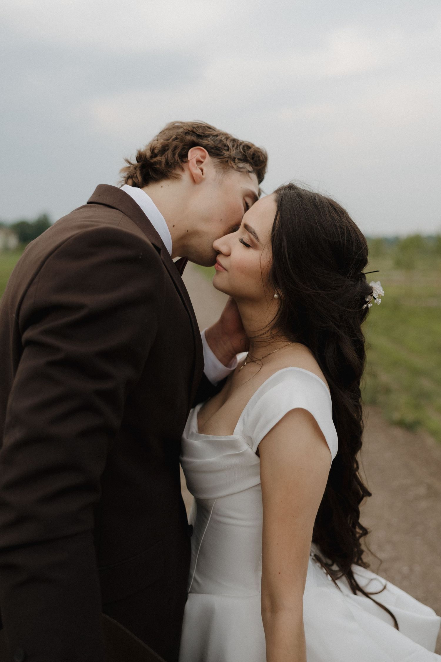 A romantic wedding couple shares an intimate kiss in a grassy field on their special day.