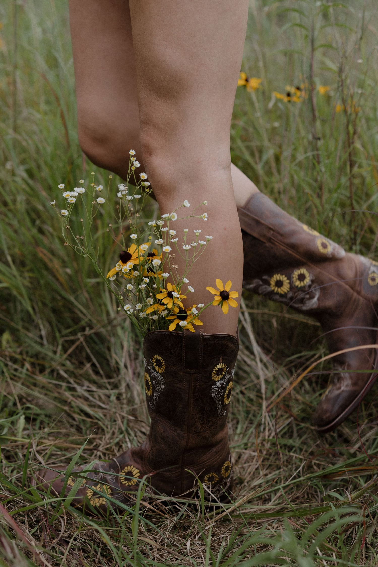 Brown cowboy boots filled with wildflowers standing in a green meadow field.
