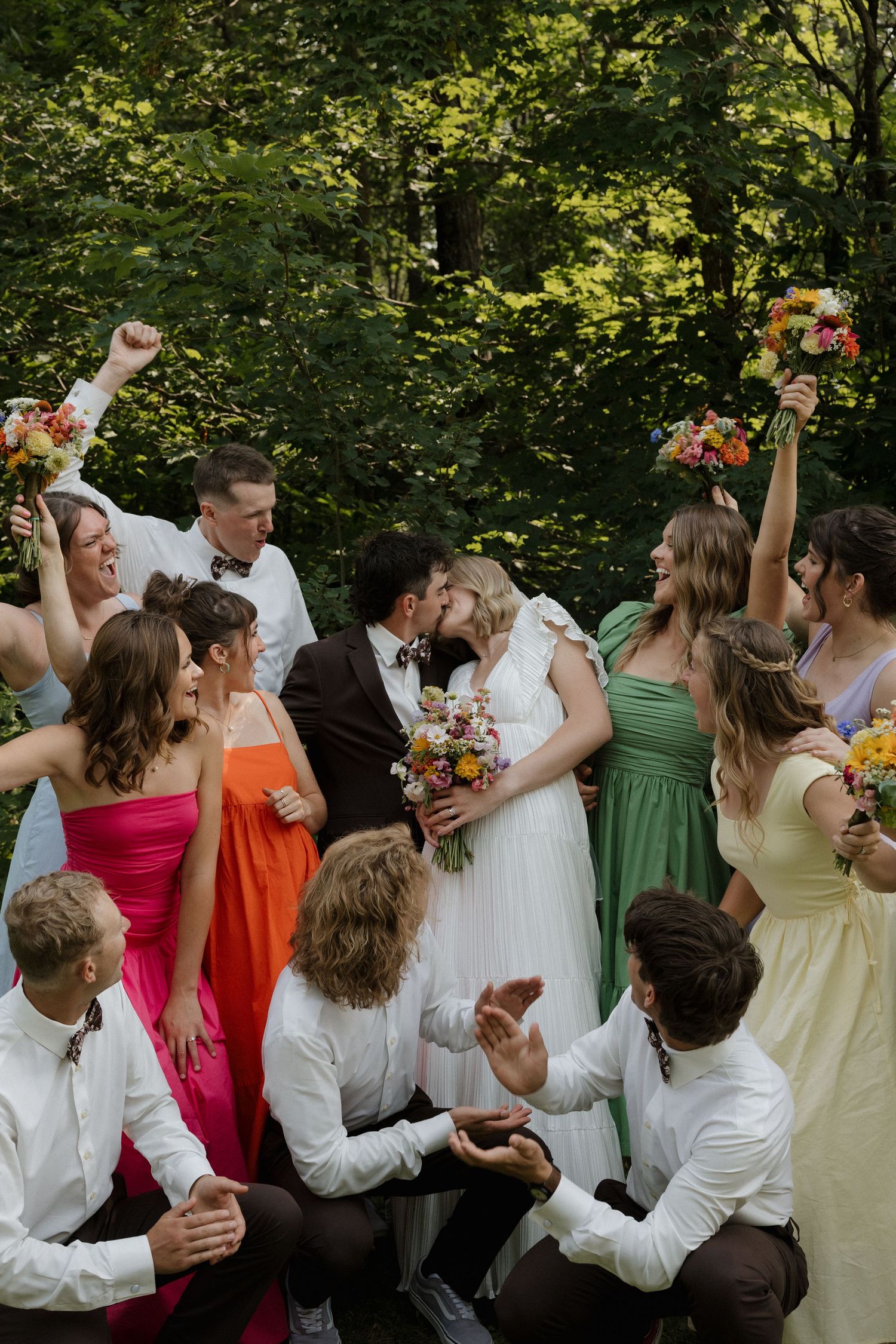 Wedding party celebrating and dancing in a line outdoors wearing colorful attire.