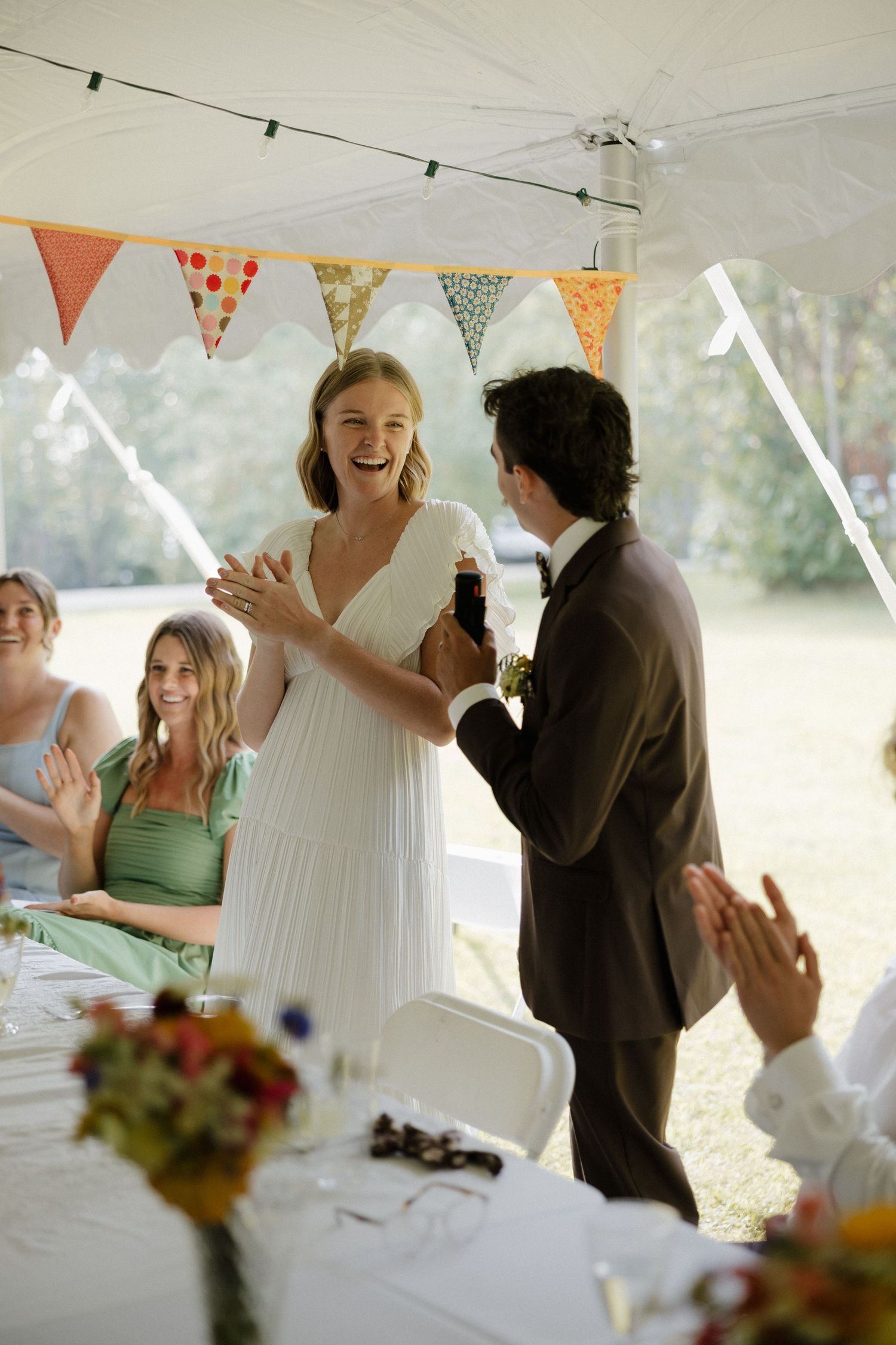 Wedding reception scene under a white tent with festive decorations and floral centerpieces.