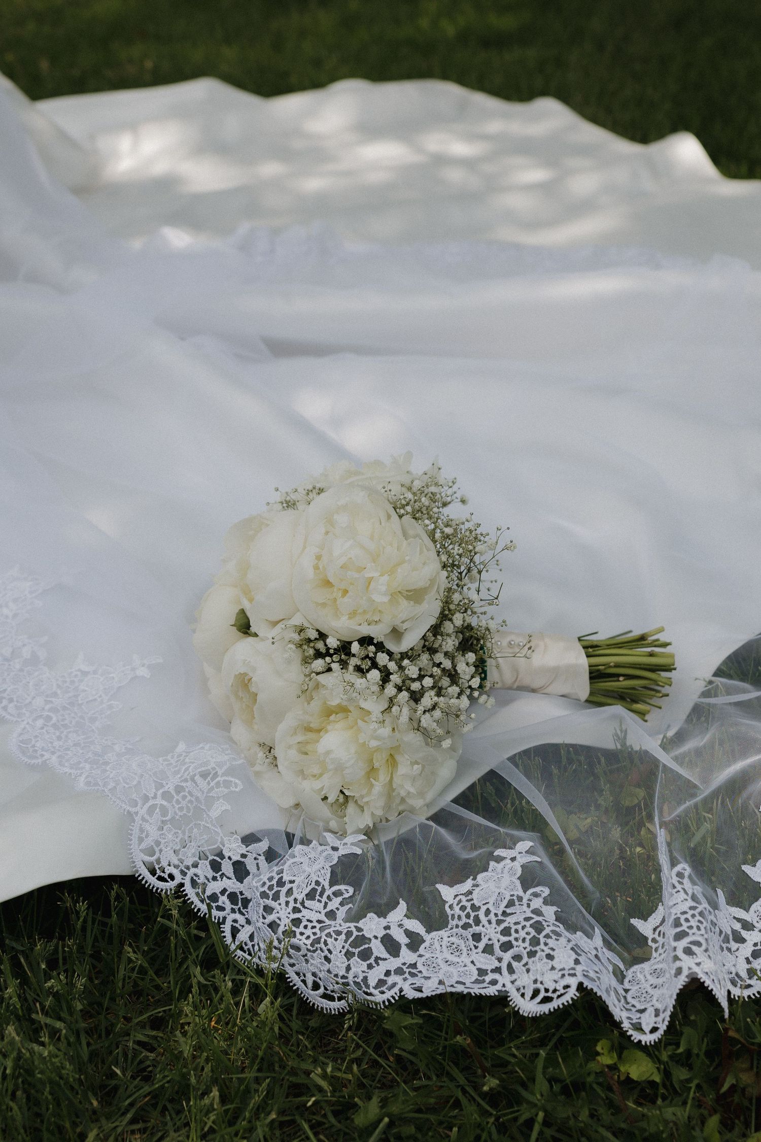 White bridal bouquet with delicate lace veil laying on grass.