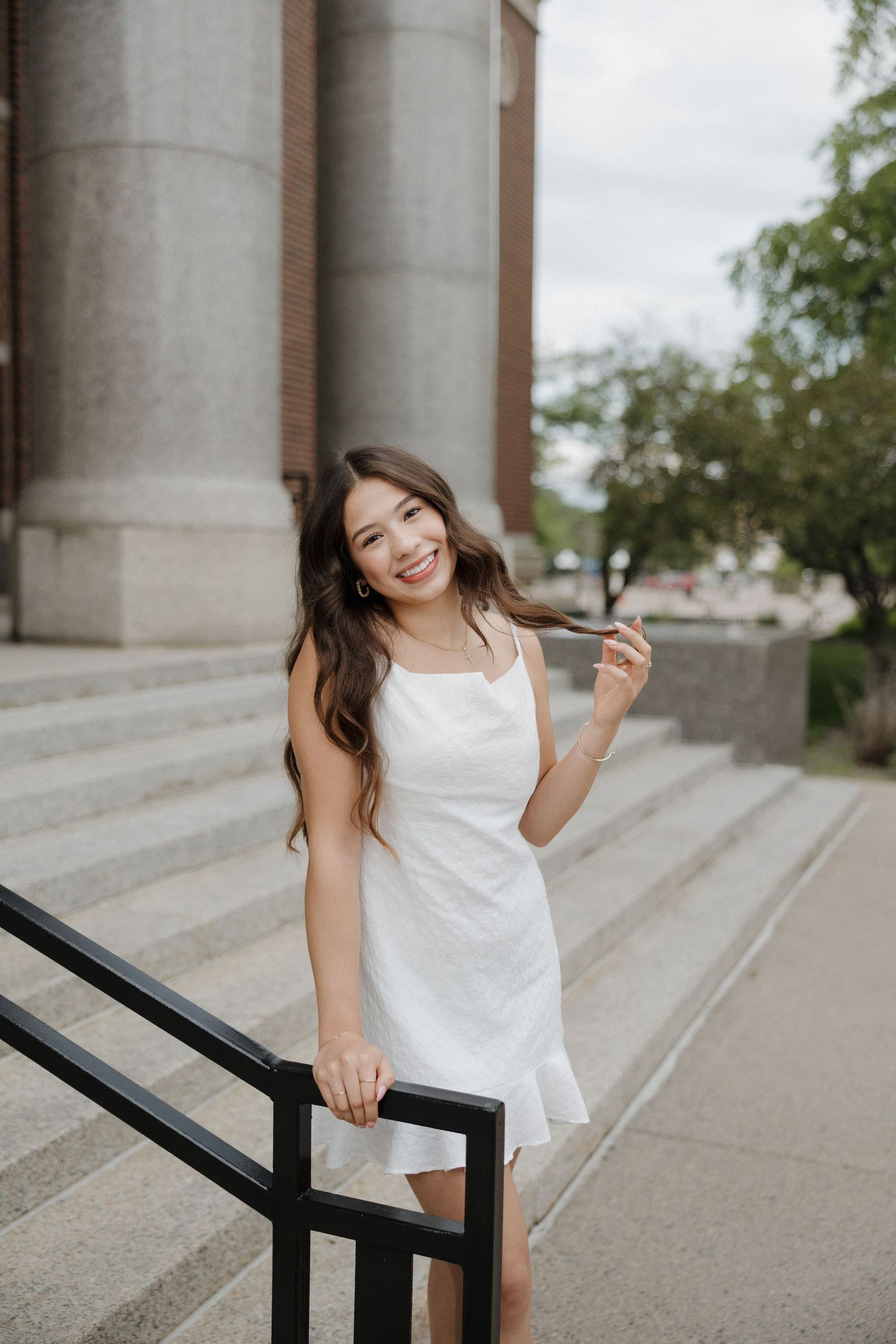 Smiling young woman in white dress posing on steps of stone building.
