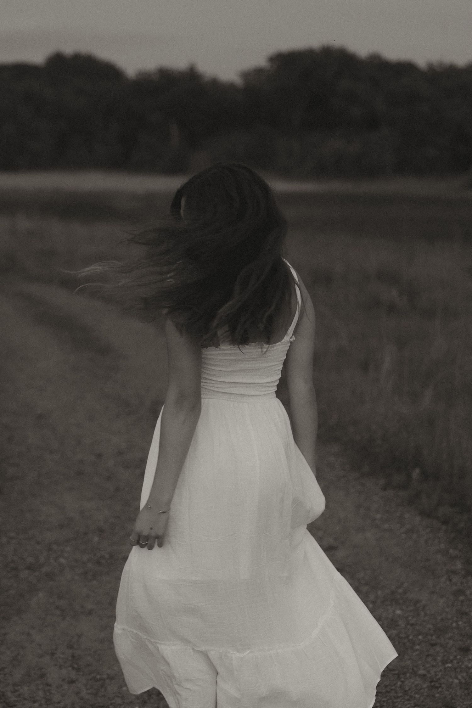 Young woman in white dress walking away on dirt road, black and white.