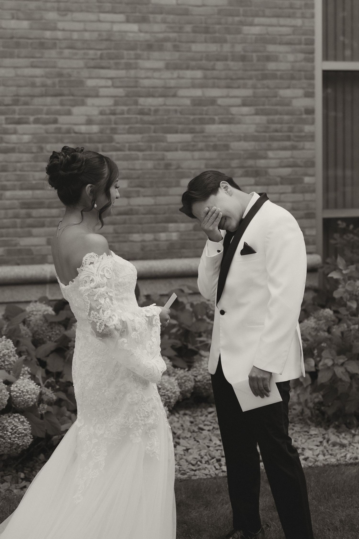 Black and white photo of newlyweds in an intimate moment by a brick wall.