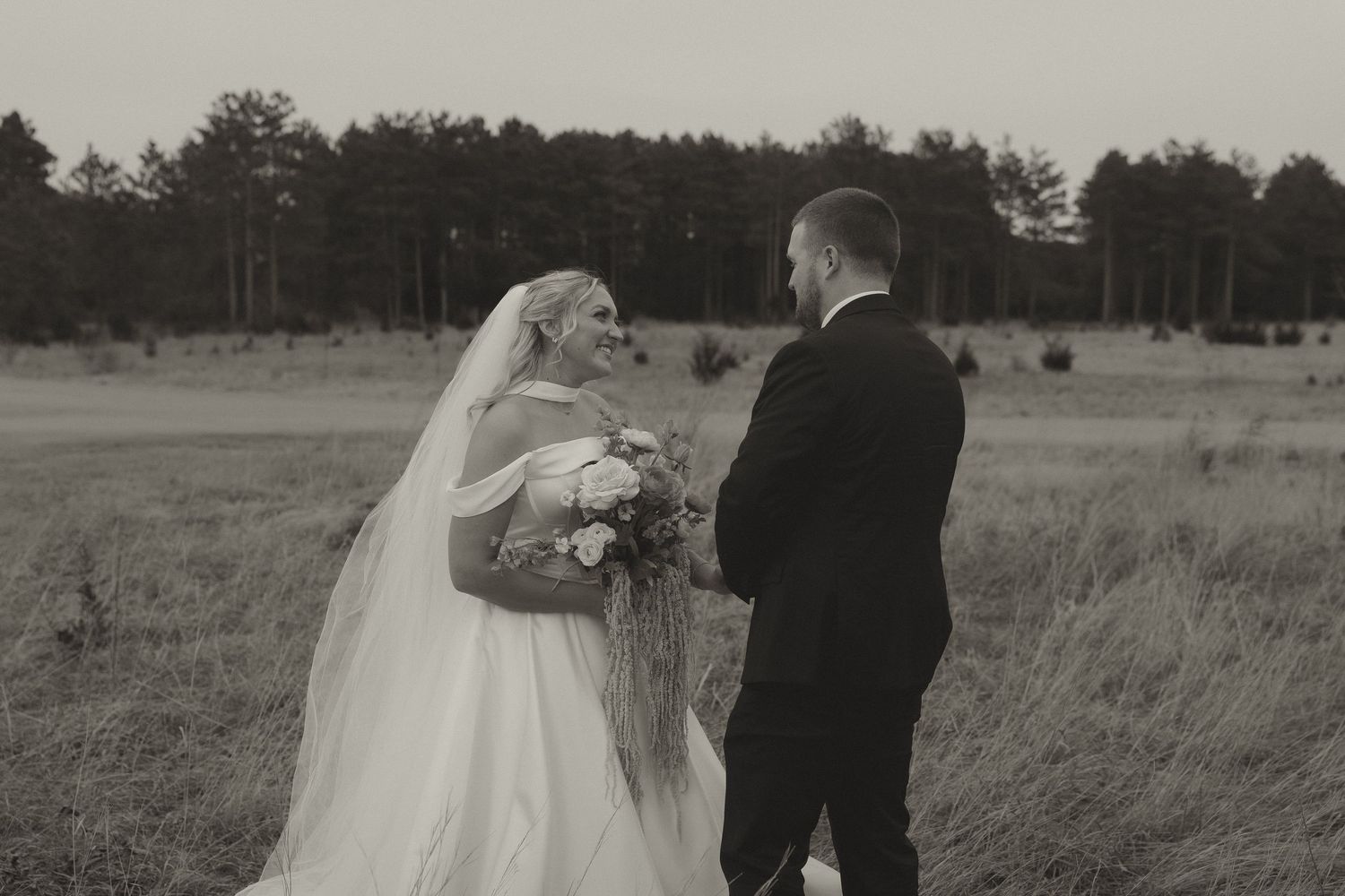 Black and white photo of a bride and groom sharing a romantic moment in a field with trees in the background.