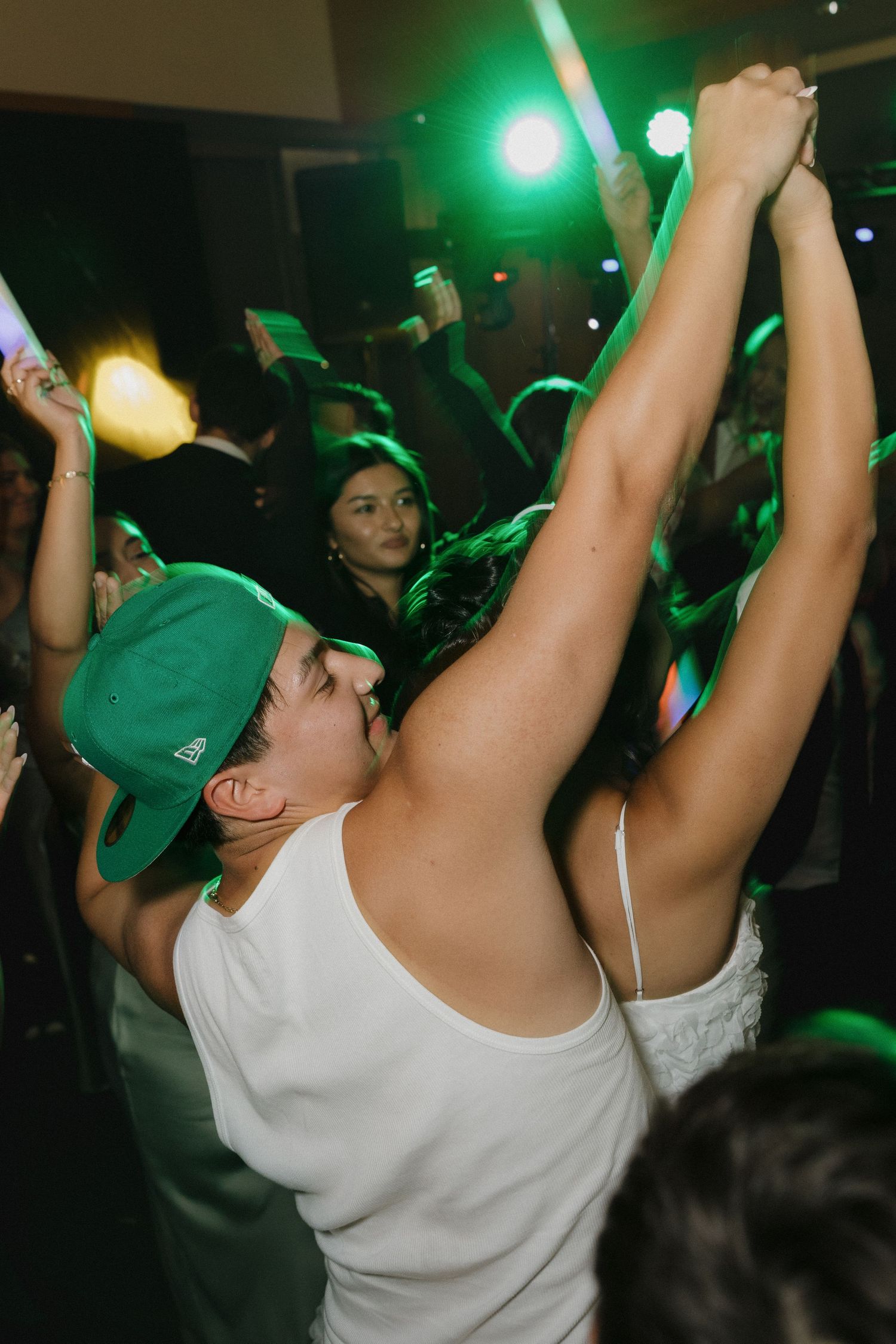 Party guests dancing with hands in the air under green lighting.