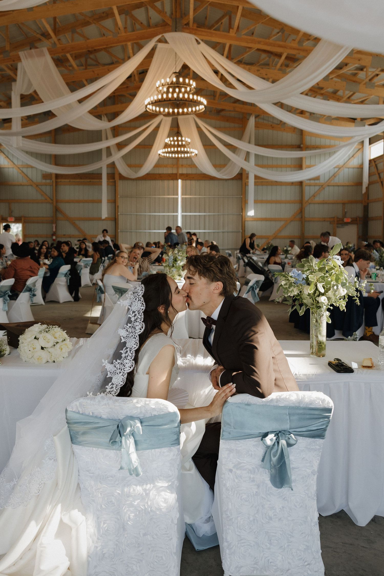 An elegant wedding reception venue decorated with white draping and chandeliers features tables set for guests.