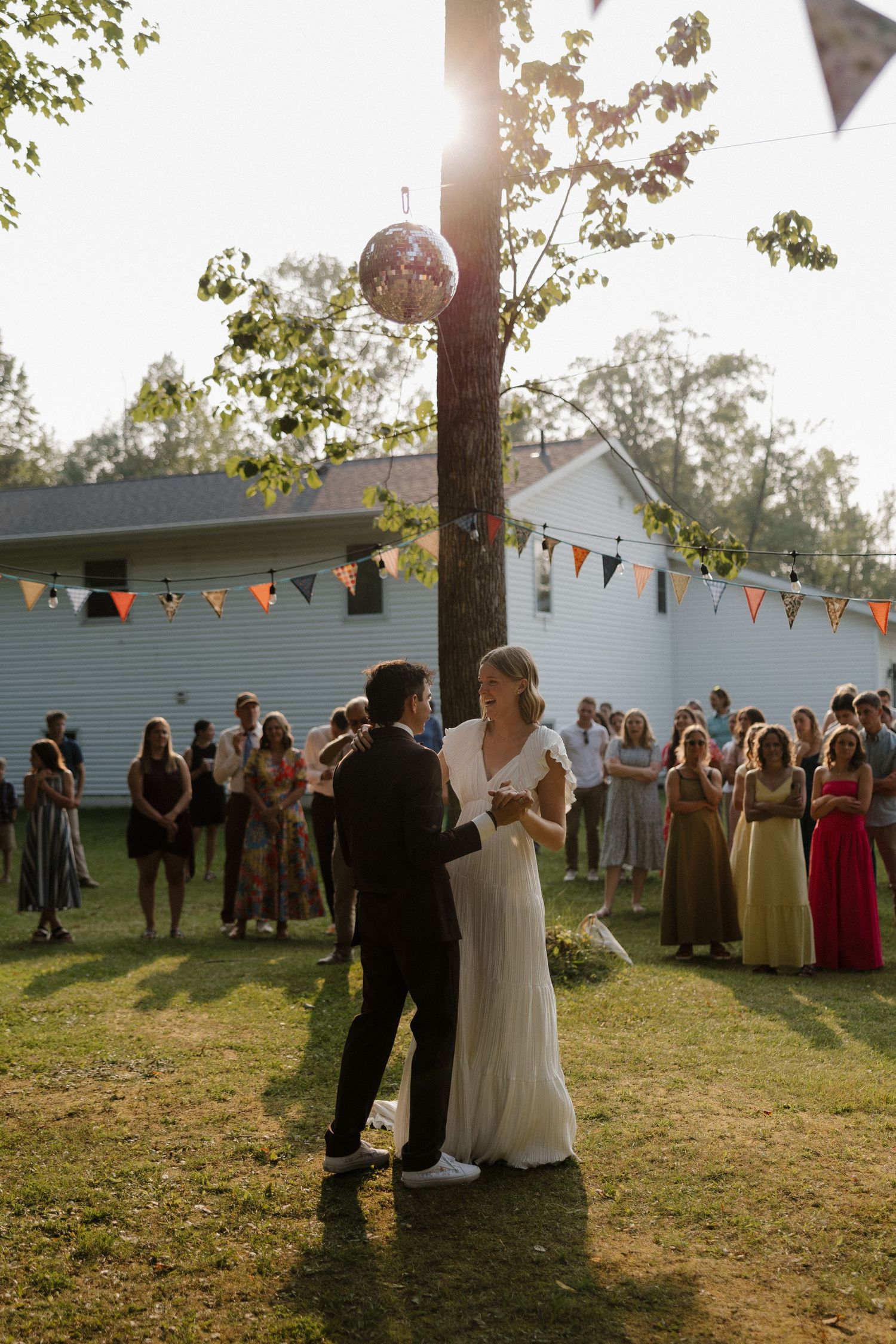 Outdoor wedding reception with string lights and bunting decorations at sunset.
