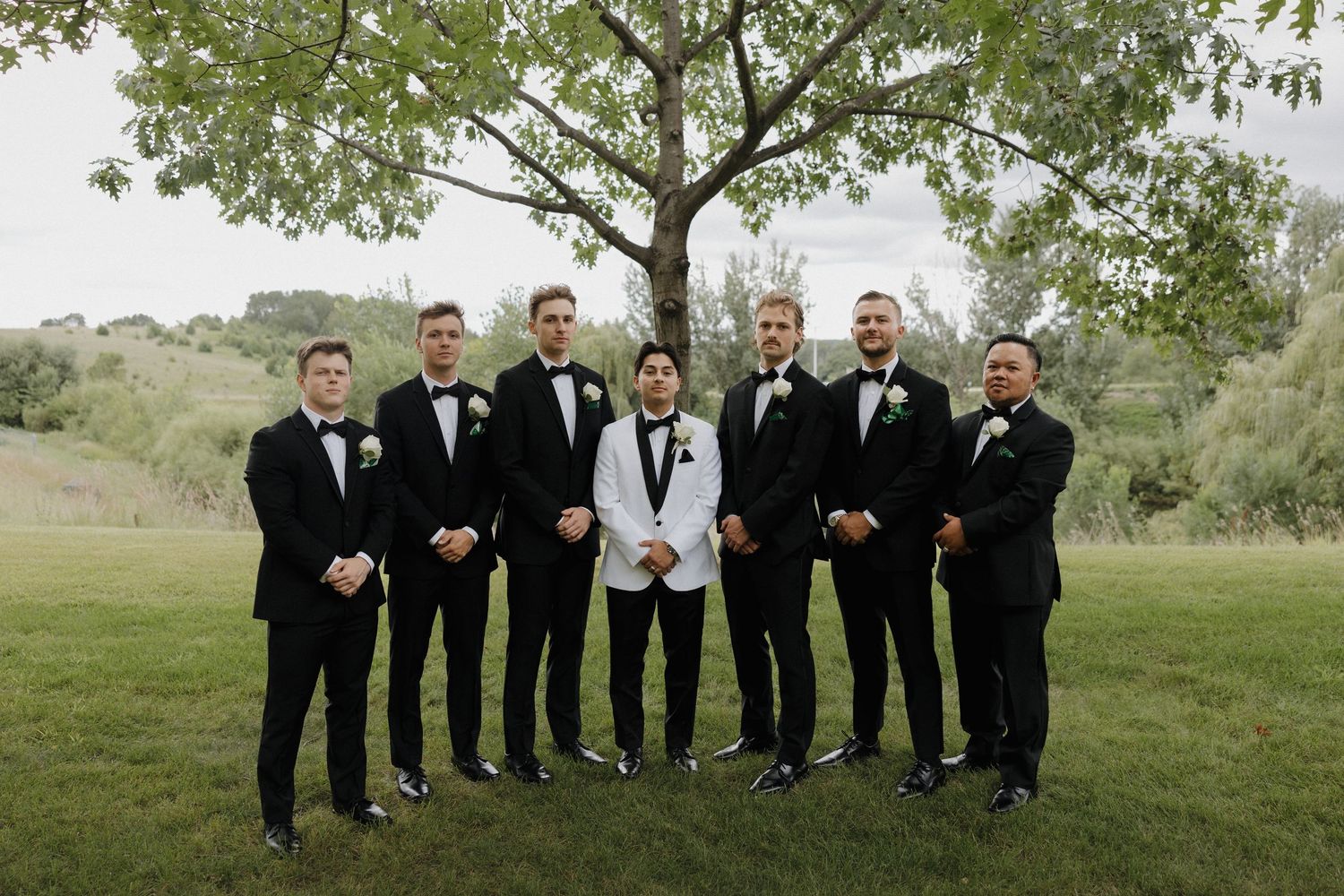 Groomsmen in black tuxedos posing casually outdoors for wedding party photos.