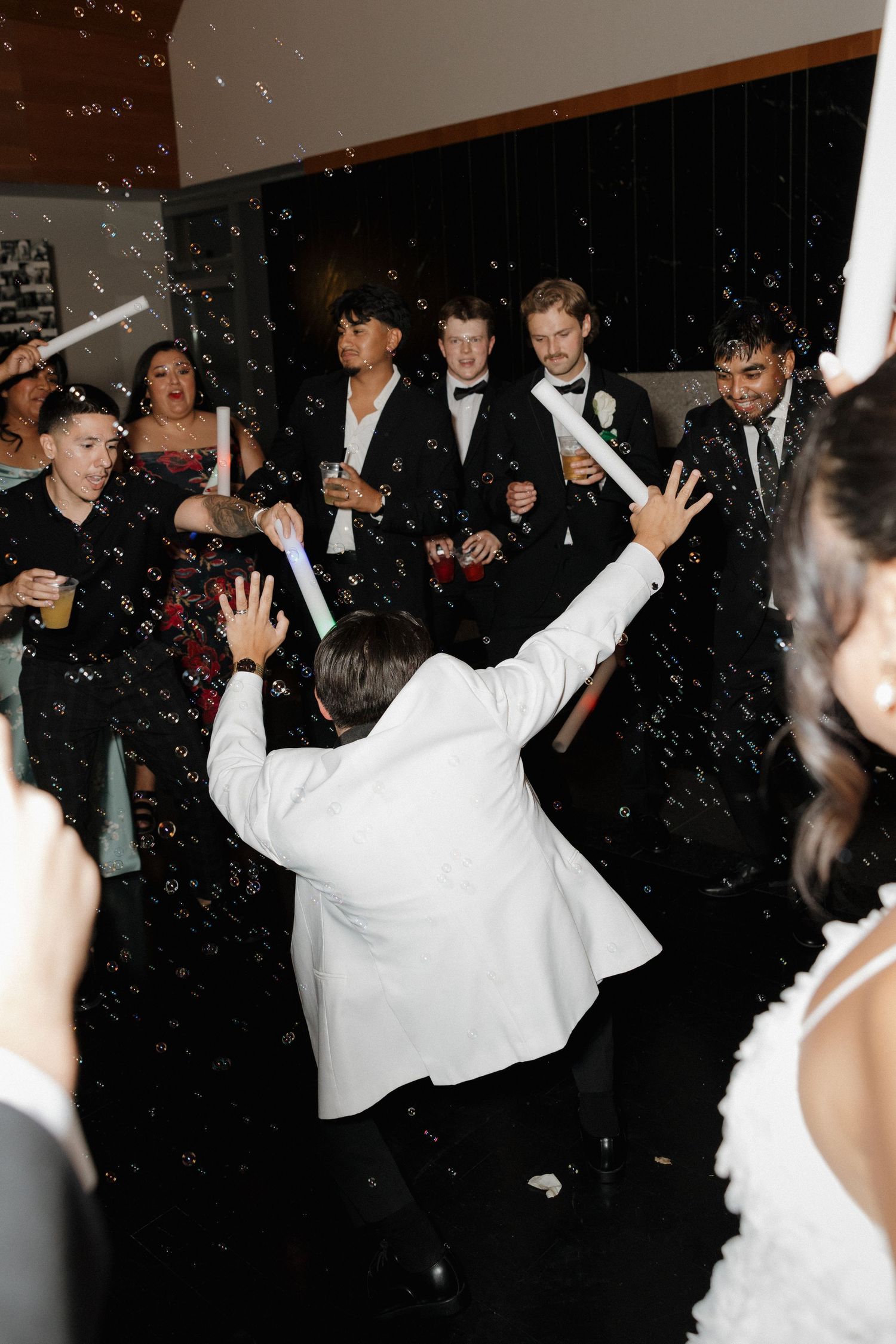 Wedding party dancing and celebrating with glow sticks on a dark dance floor during reception festivities.