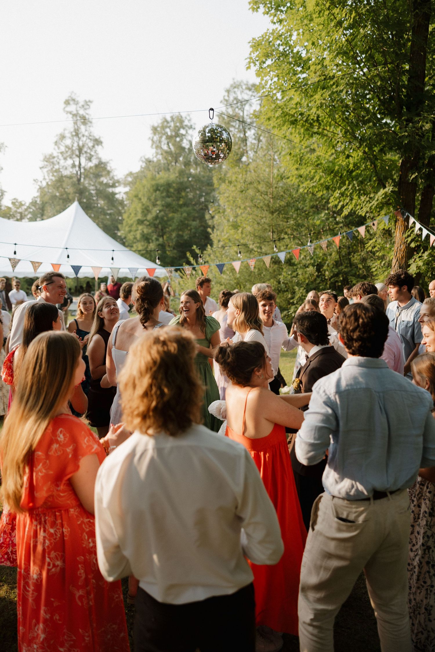 Wedding guests gather under string lights and a white tent for an outdoor reception.