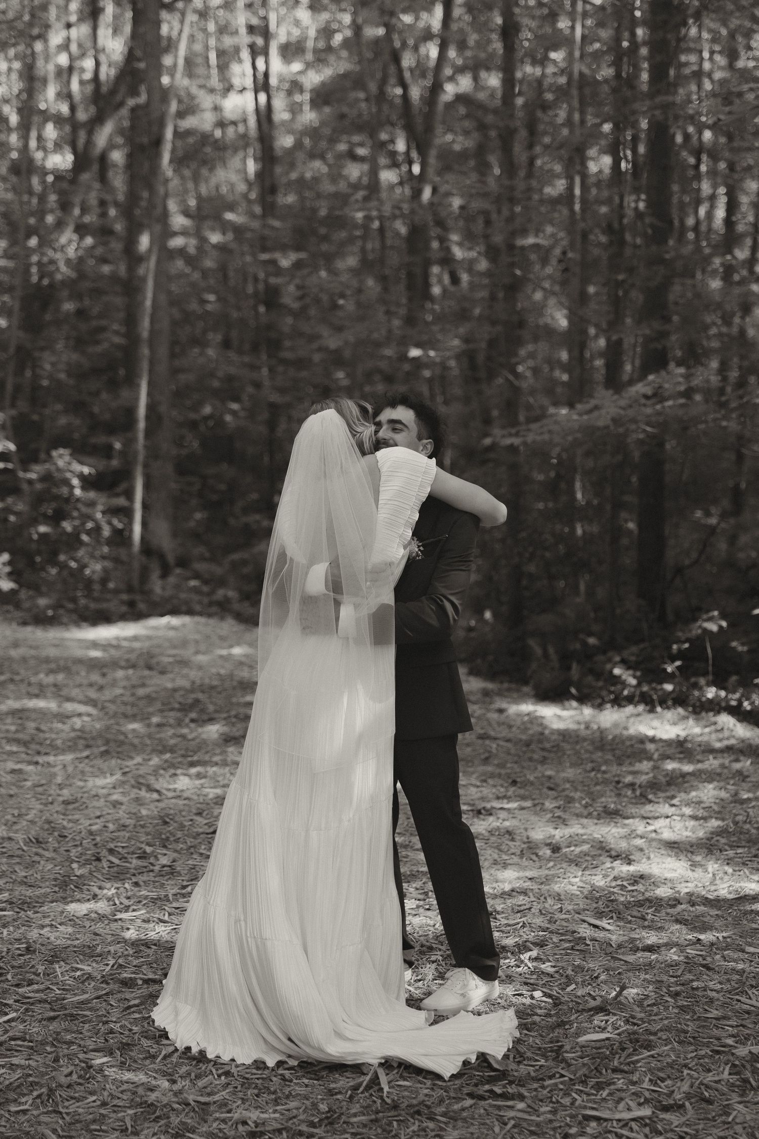A romantic black and white portrait of newlyweds embracing in a wooded setting.