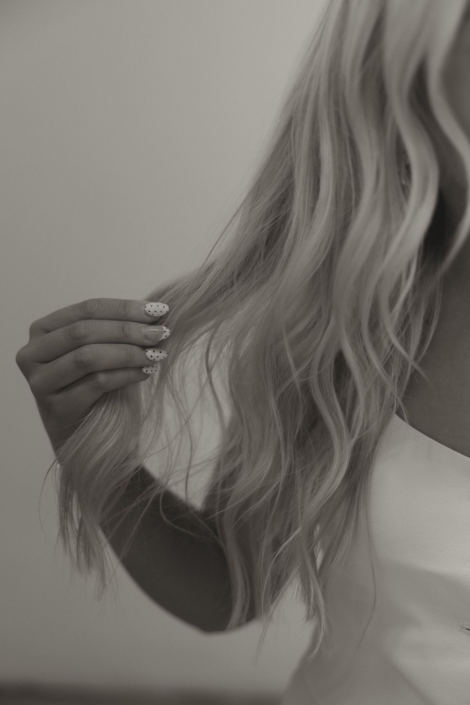 Close-up black and white photo of long blonde wavy hair being held by a hand with decorated nails.