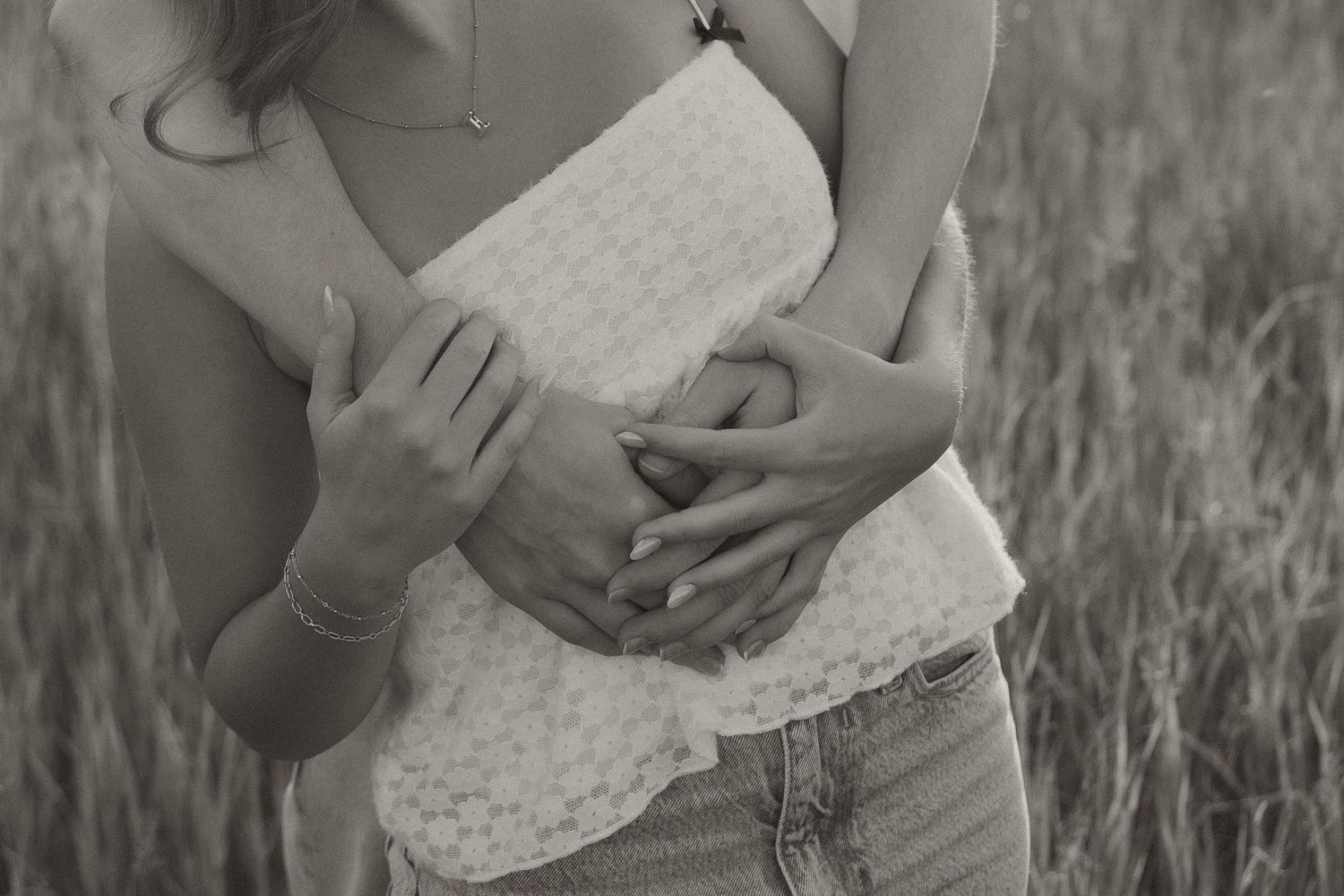 Black and white close-up of couple's hands embracing woman's waist in lace top and jeans.