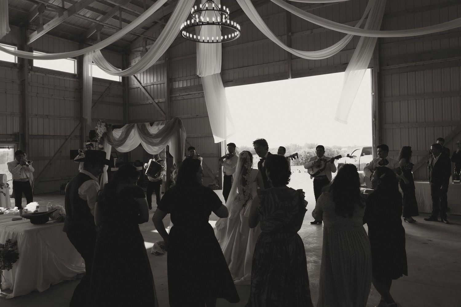 Black and white silhouettes of wedding guests mingling under draped fabric at an indoor reception.