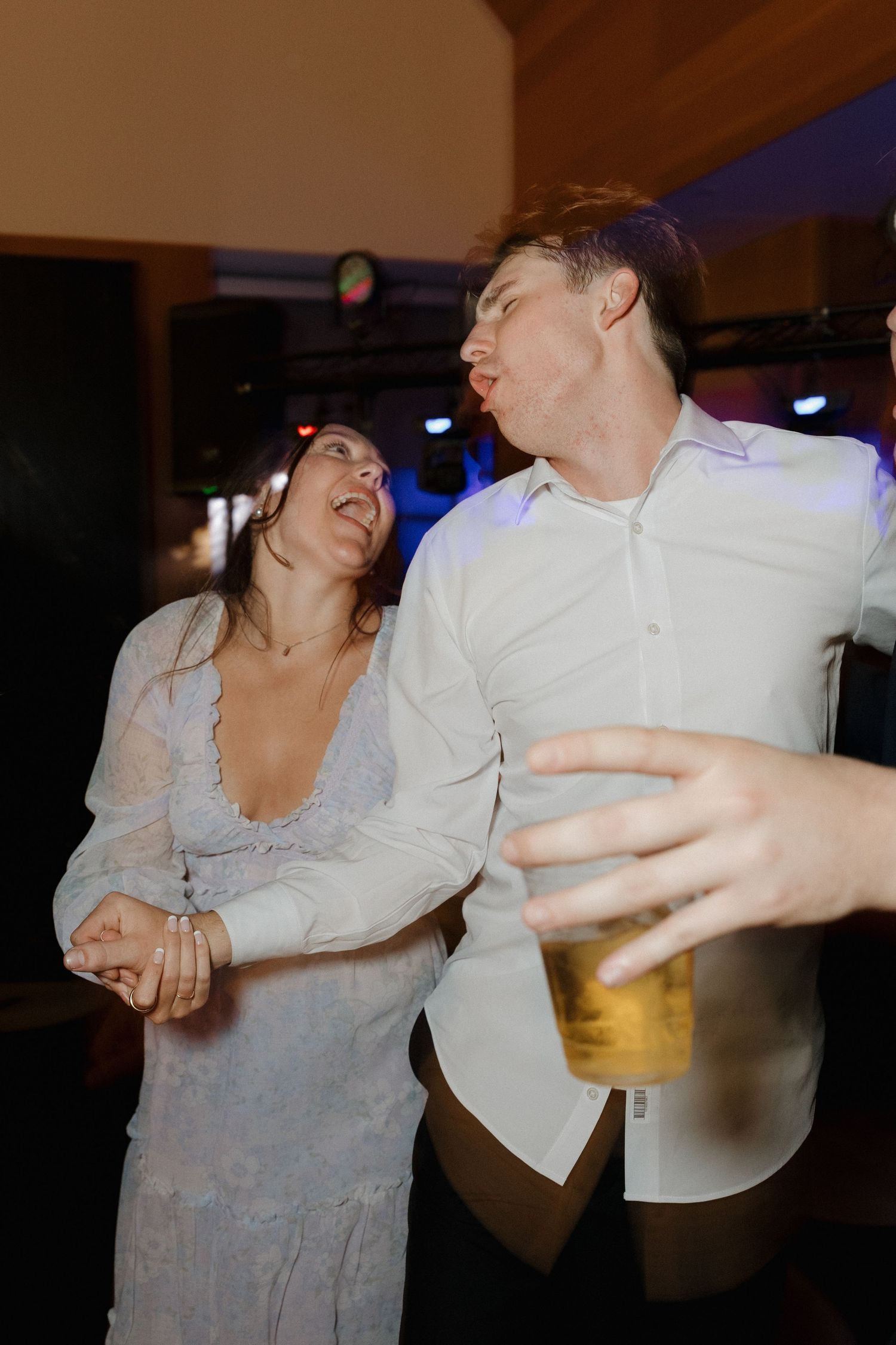 Candid moment of dancing and laughter at a wedding reception with a beer in hand.
