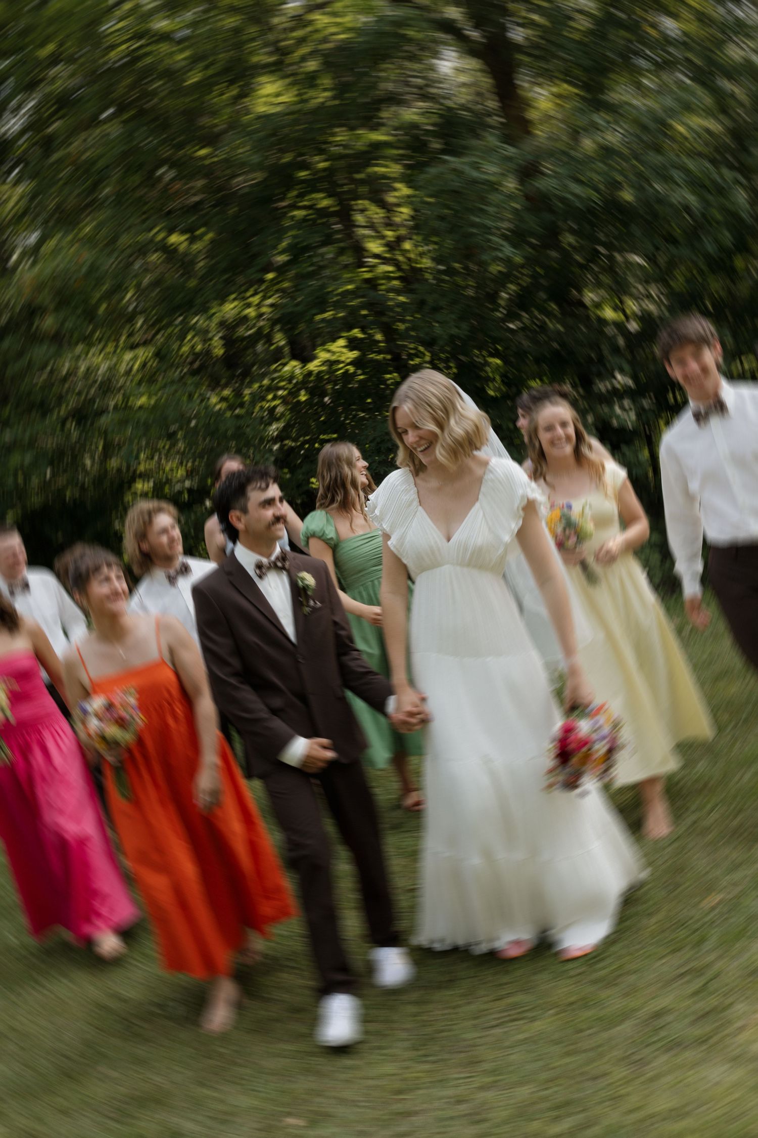 Motion-blurred photo of wedding party dancing in a line wearing bright dresses.