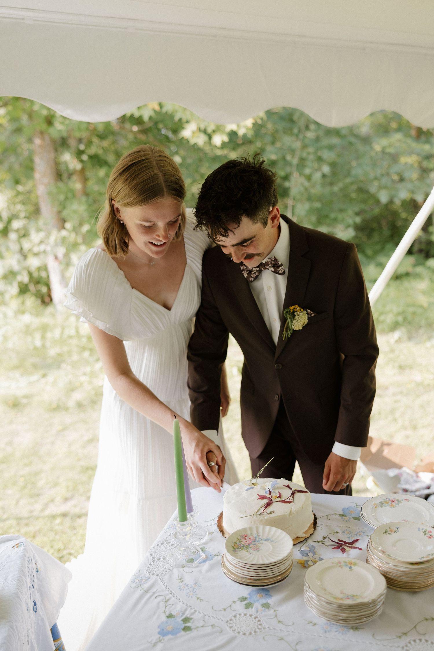Wedding couple cutting cake together at outdoor reception table.