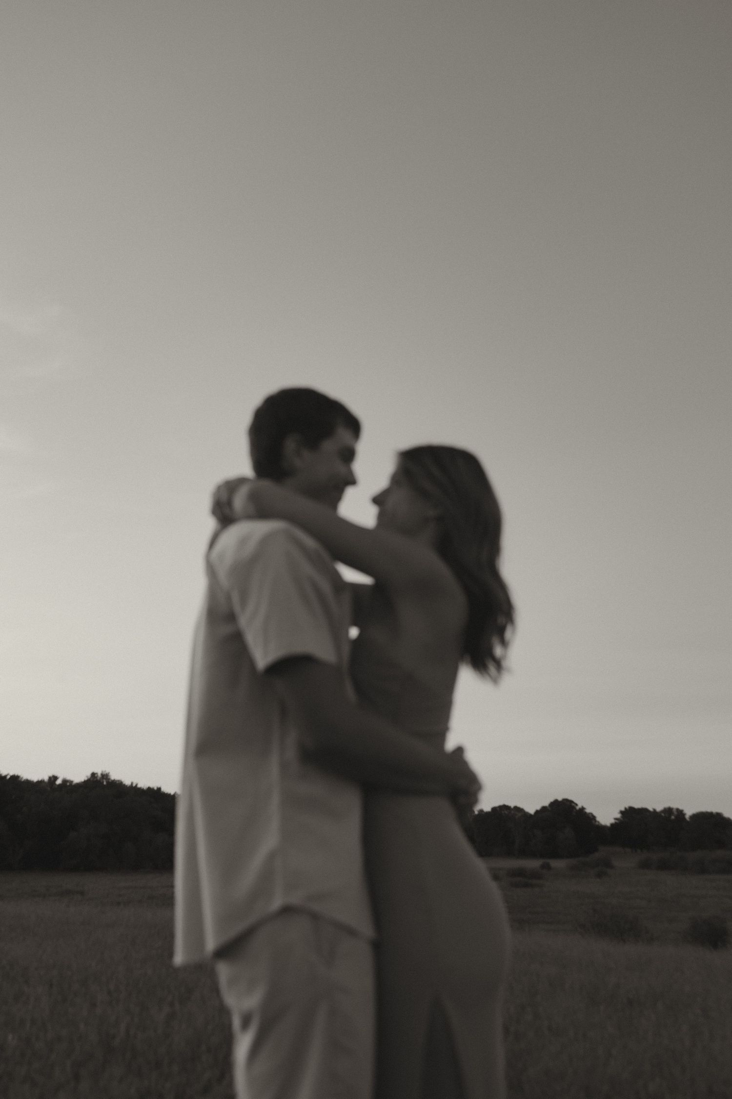Romantic black and white silhouette of a couple embracing in an open field at dusk.