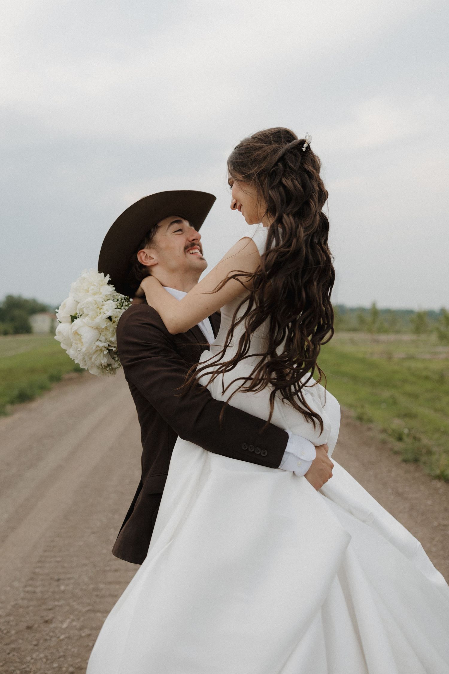 A romantic wedding couple shares a playful dip kiss on a country road.