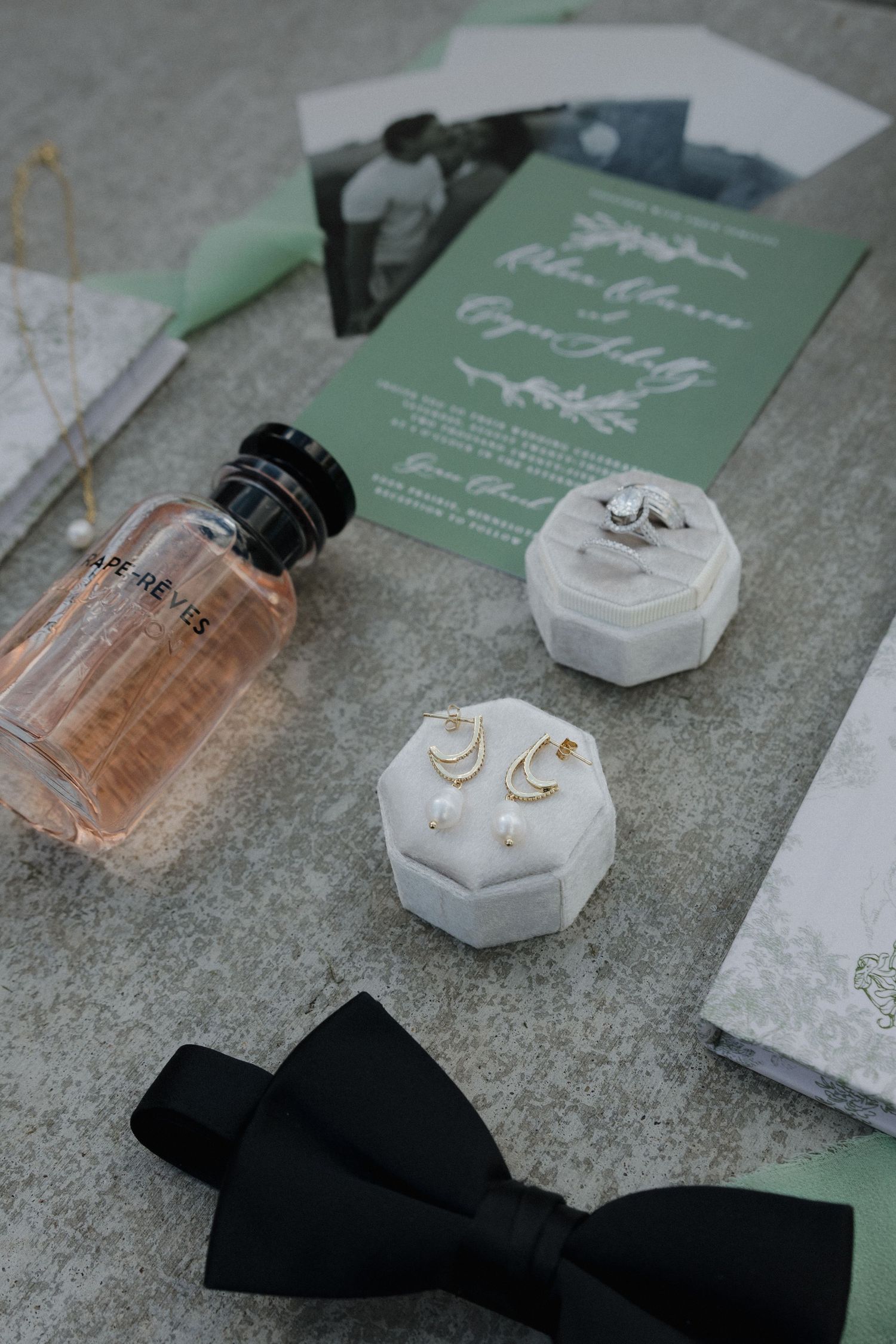 Wedding accessories including invitations, perfume bottles, and jewelry arranged on gray surface.