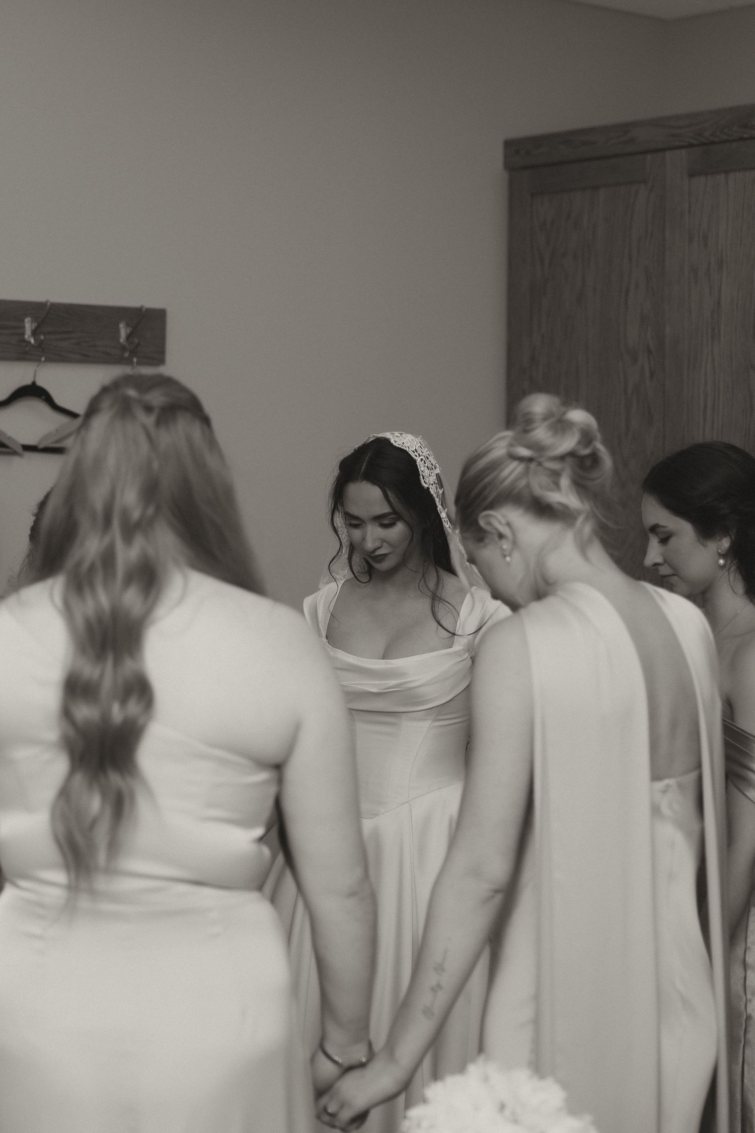 Bridesmaids in matching white dresses huddle together in preparation for a wedding ceremony.