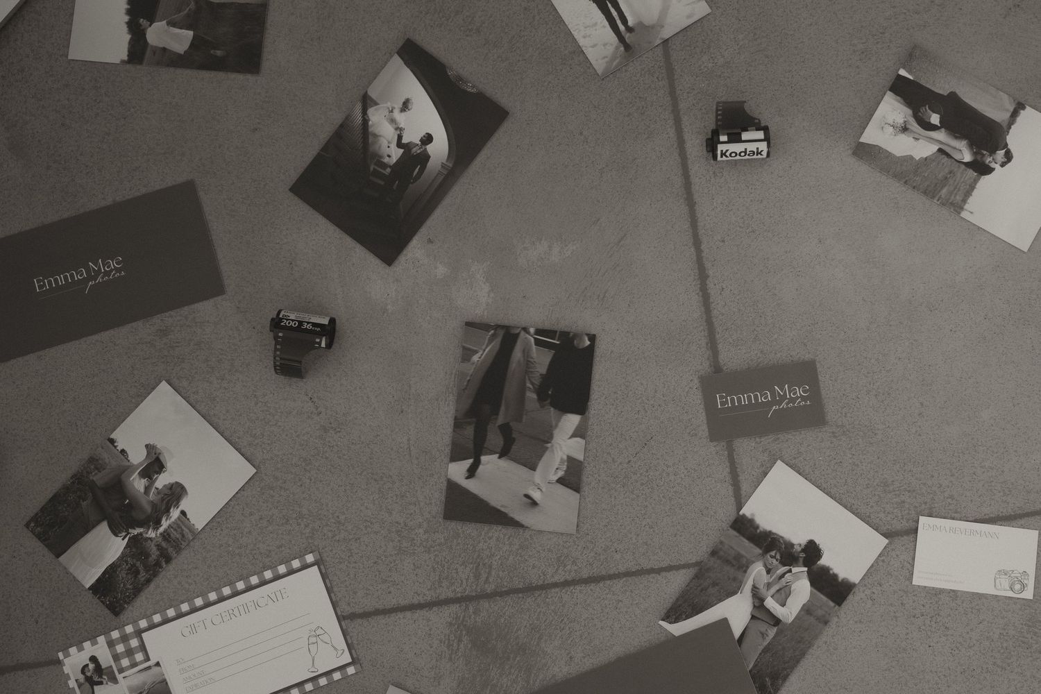 Overhead black and white flat lay of Emma Mae Photos branding materials and film cameras on floor.
