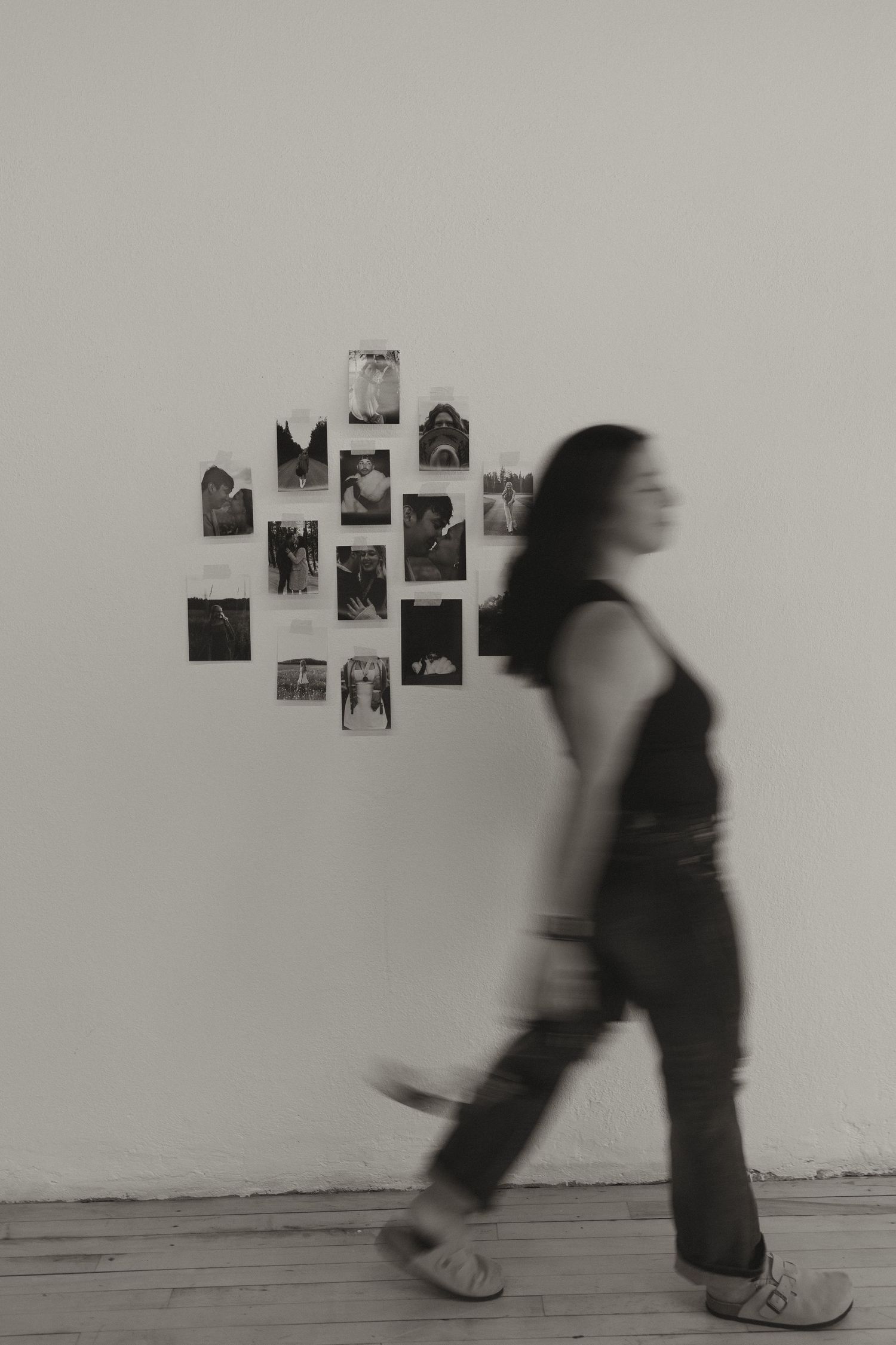 Black and white motion blur photo of woman walking past a wall display of black and white photographs.