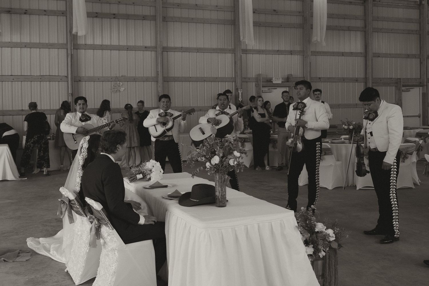 Musicians with guitars perform at an indoor event around a decorated table in a black and white photograph.