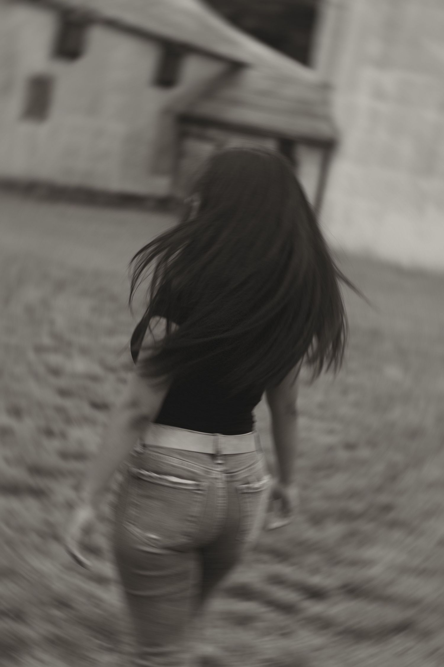 Black and white photo of young woman with flowing dark hair walking away in shorts outdoors.