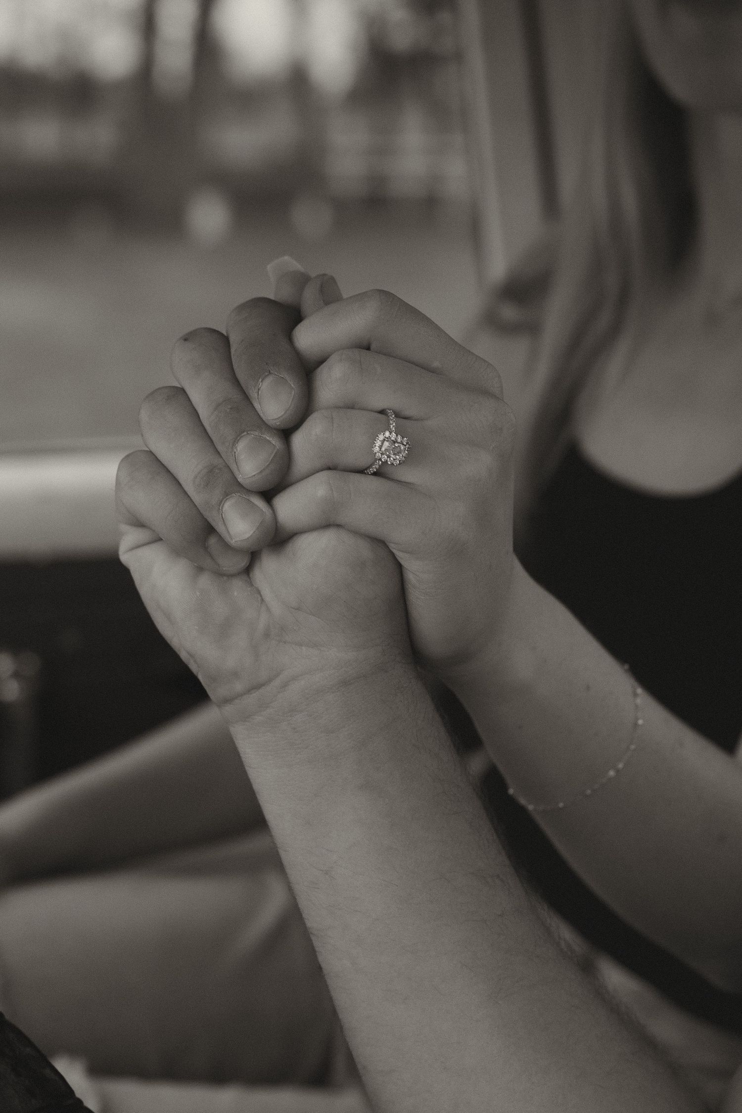 Black and white close-up of couple holding hands, woman wearing diamond engagement ring.