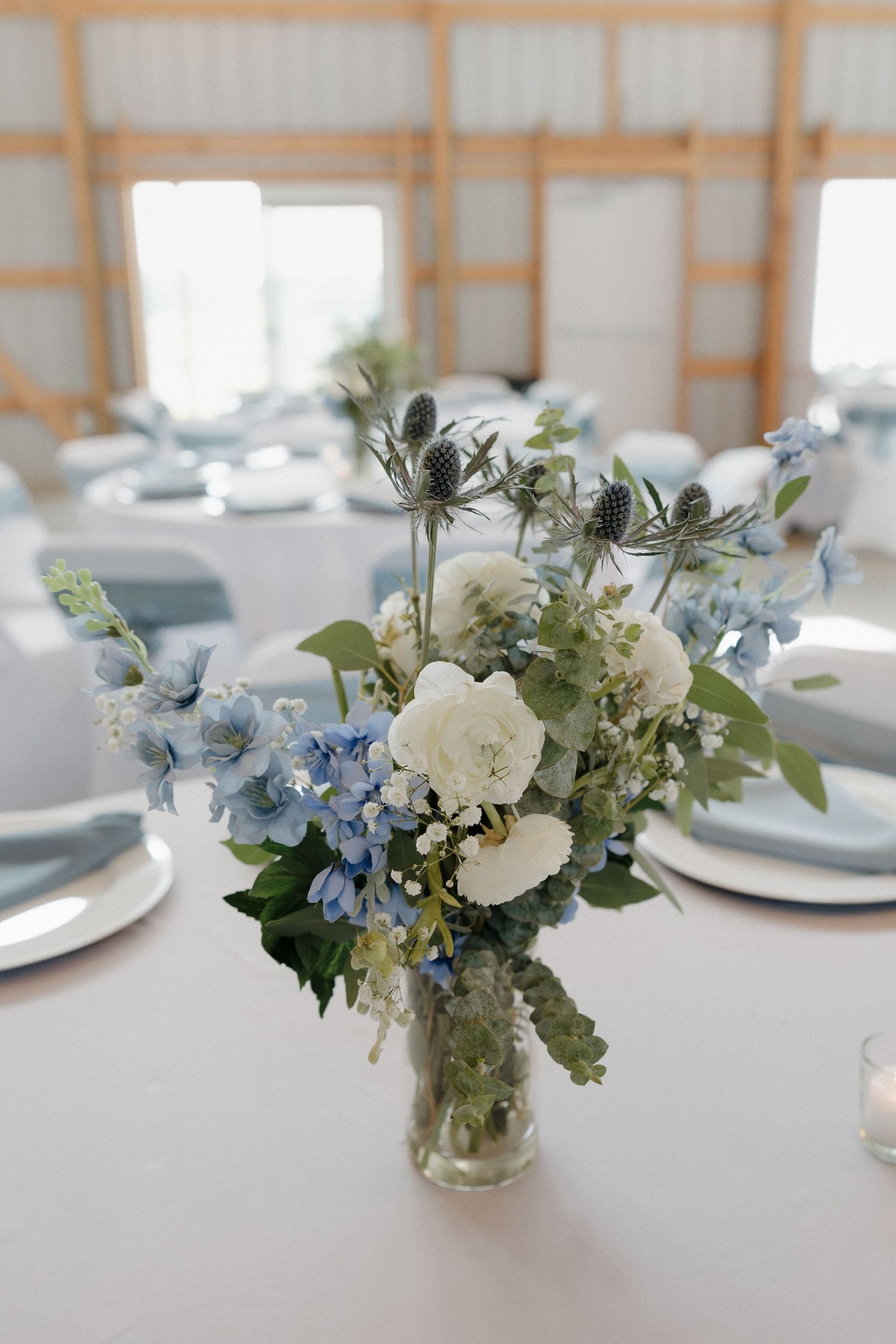 Elegant wedding centerpiece featuring white roses and light blue hydrangeas in a glass vase on a white tablecloth.