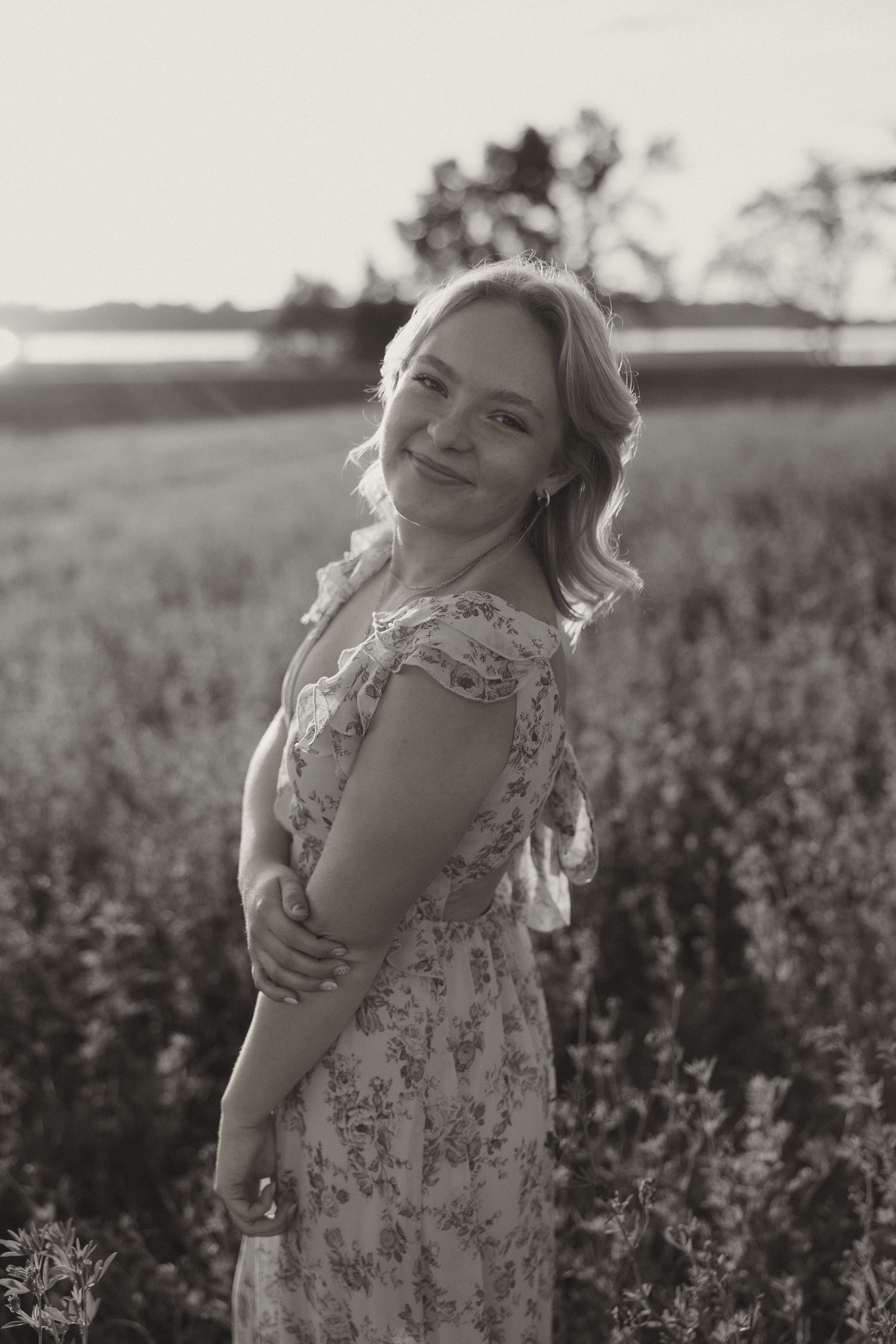 Black and white portrait of blonde woman in floral dress in field at sunset.