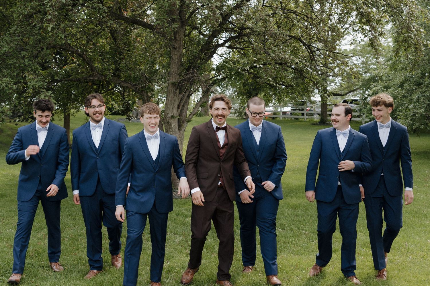 Groomsmen in navy blue suits walking together outdoors in a natural setting for wedding photos.