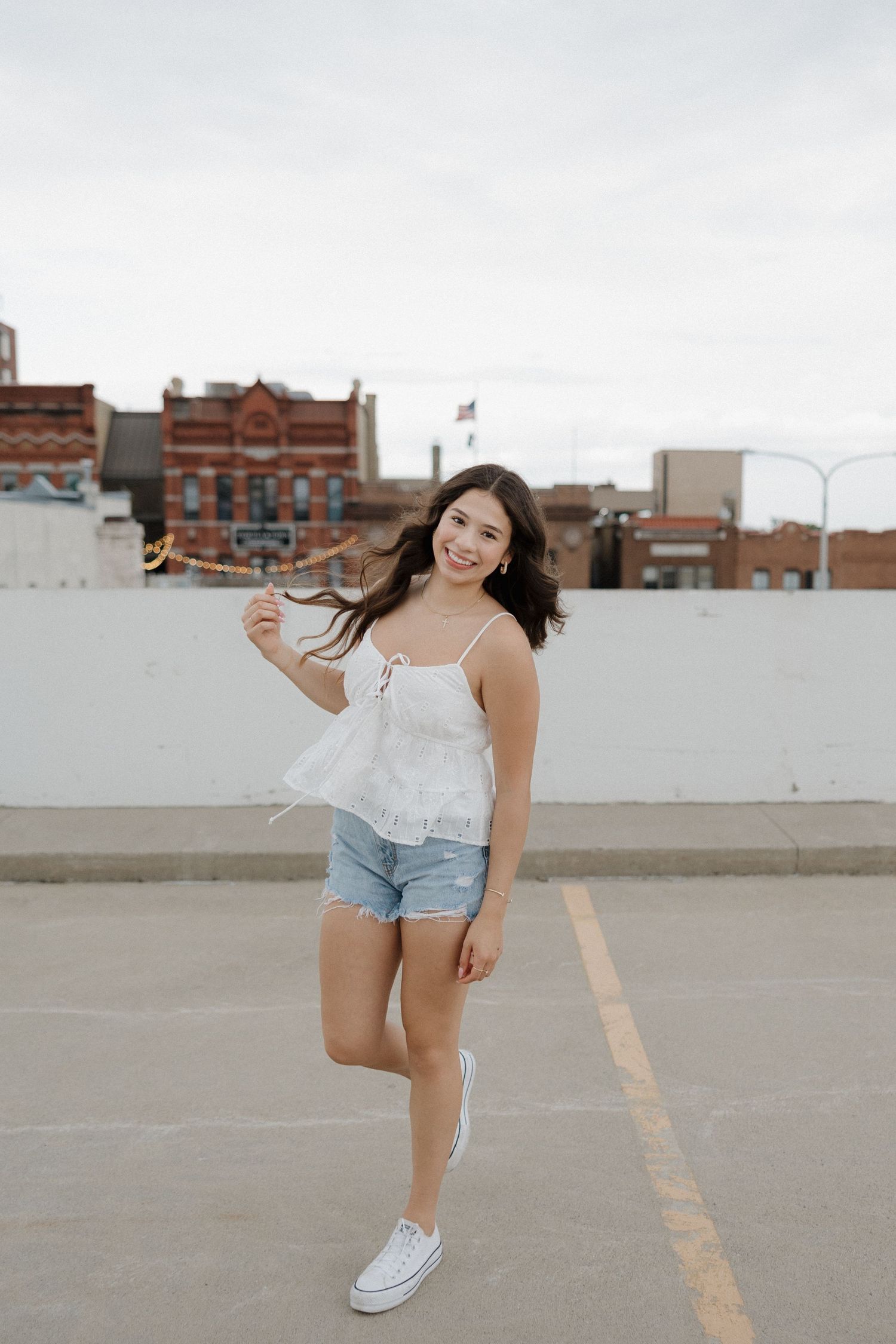 Smiling young woman in white top and denim shorts on rooftop parking lot.