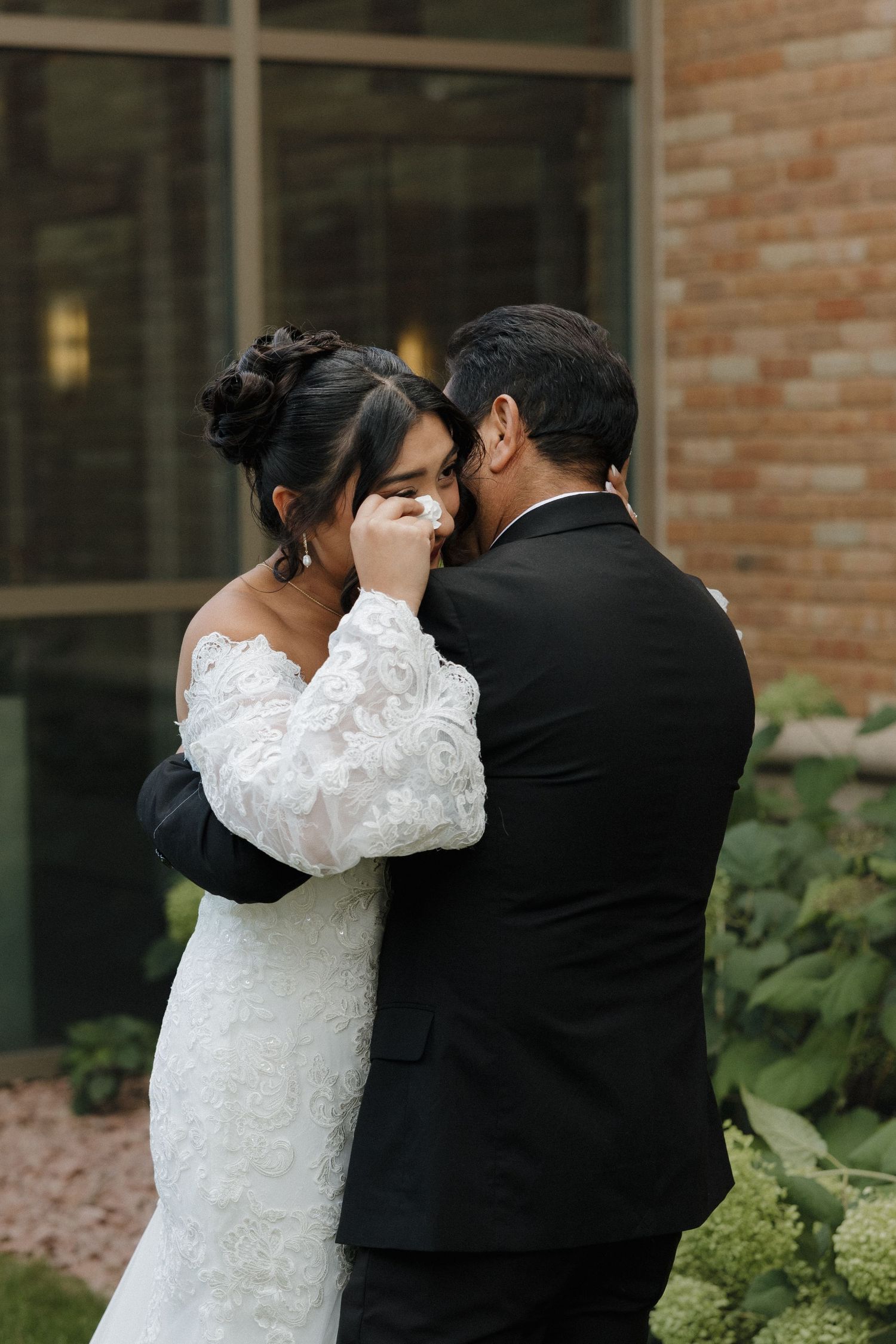 Couple sharing an intimate moment in wedding attire against brick building backdrop.