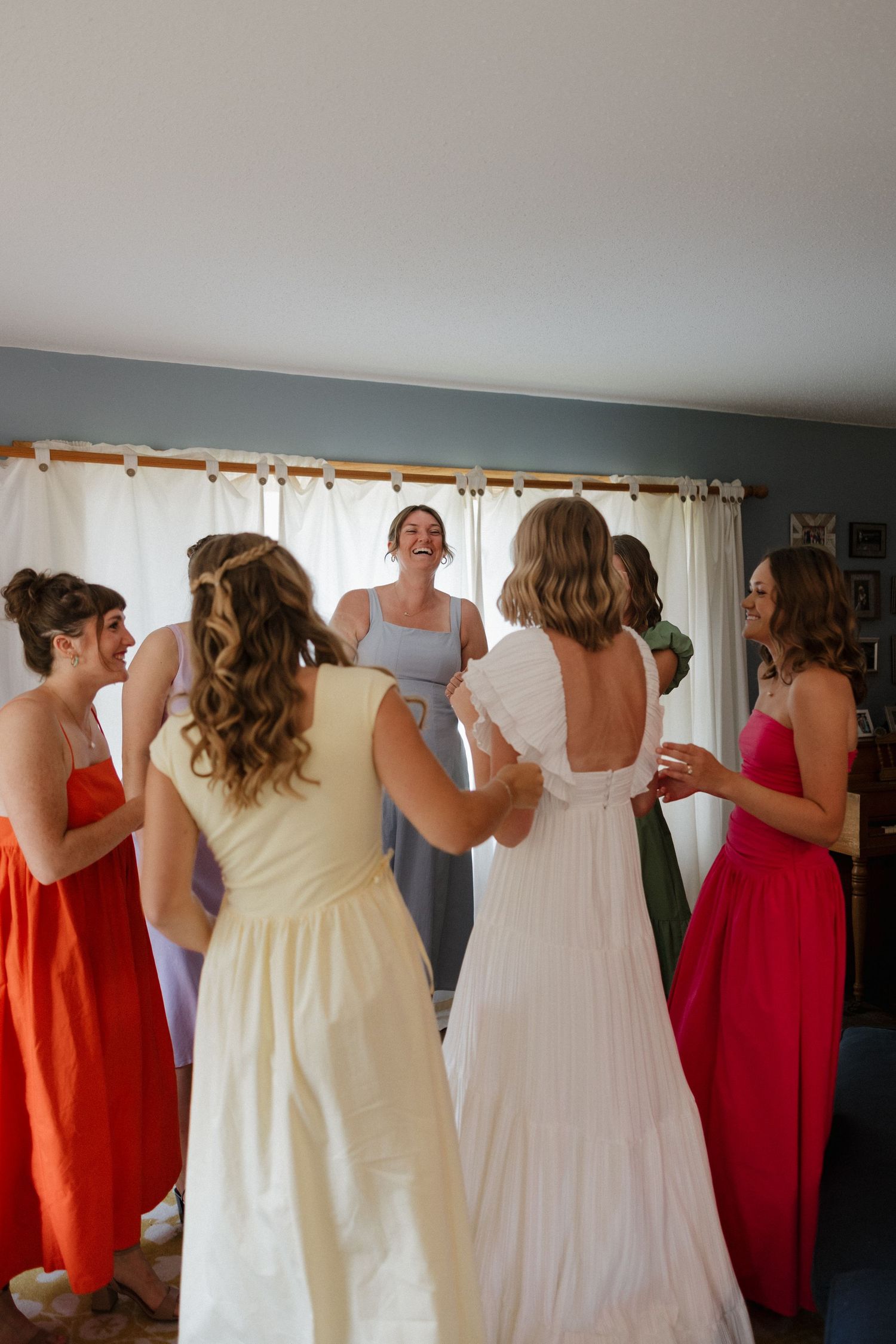 Bridesmaids in red dresses help the bride get ready in a sunlit room.