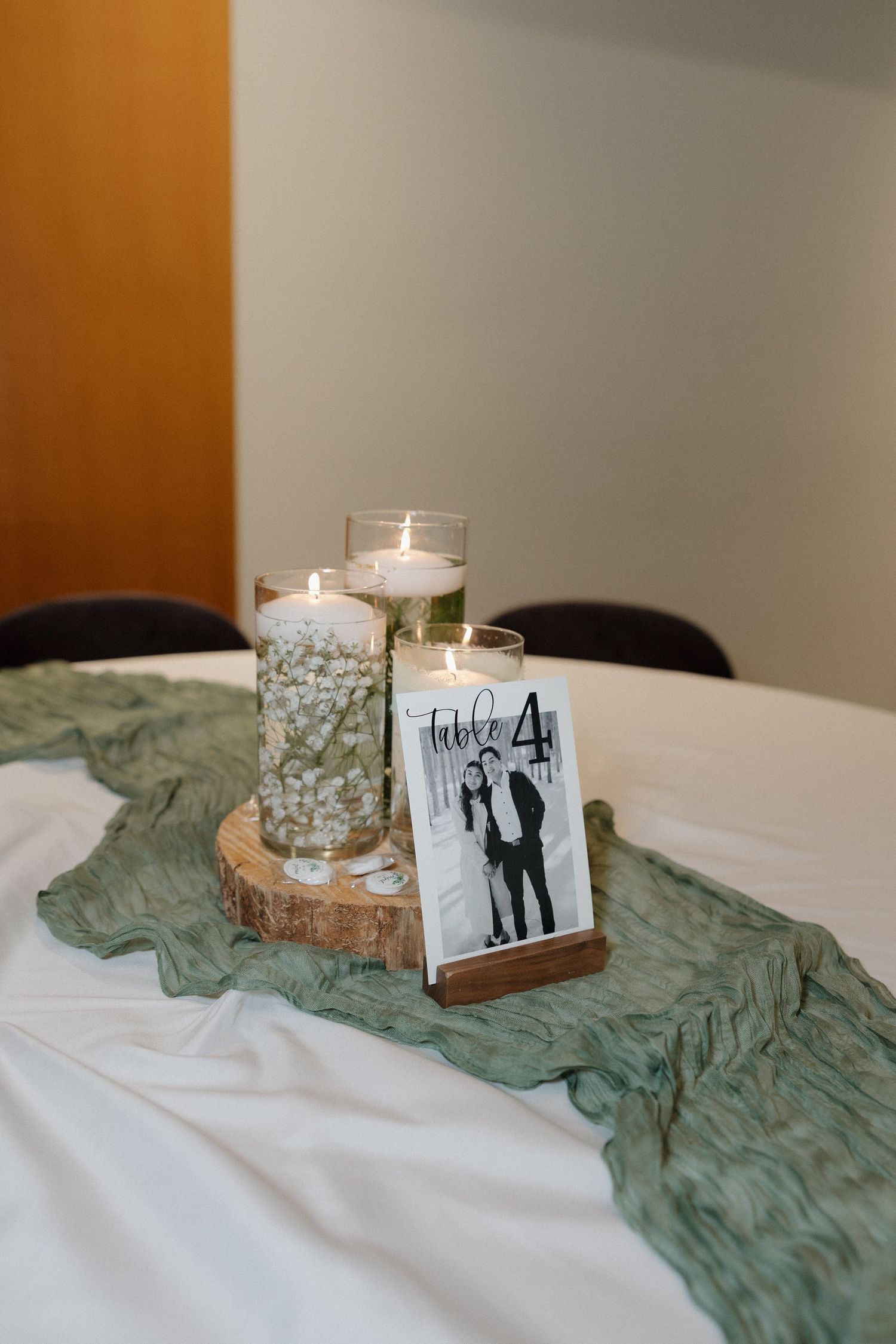 Wedding reception table decor featuring candles in glass holders with a soft sage green fabric runner.