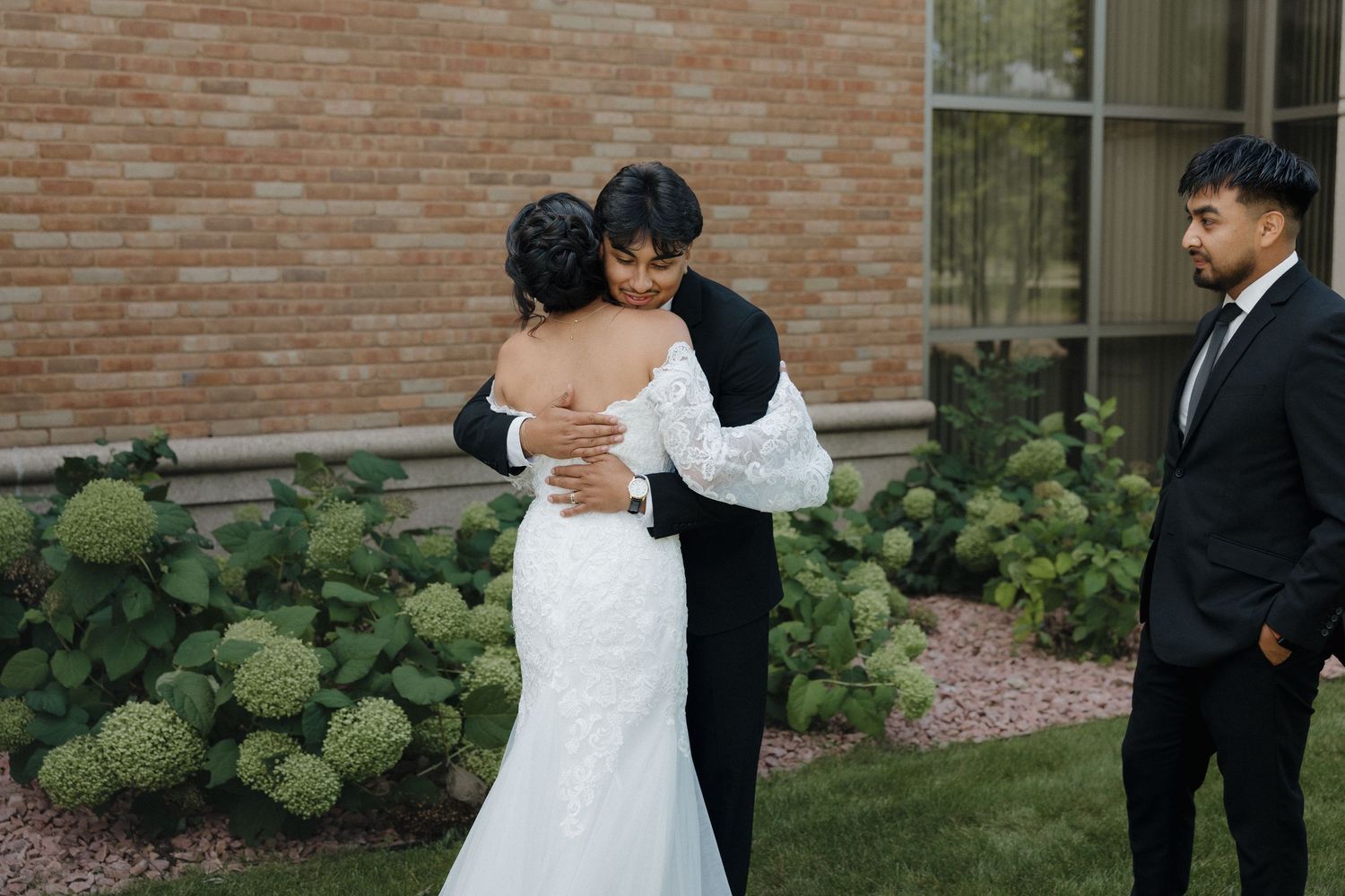 Couple in wedding attire standing together outside brick building.