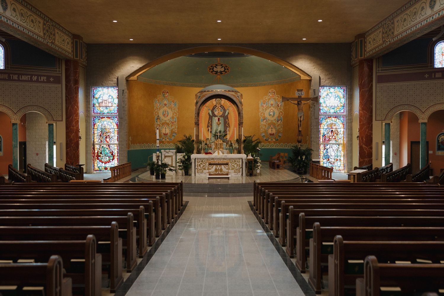 Panoramic view of an empty church interior with wooden pews and stained glass windows illuminating the sanctuary.
