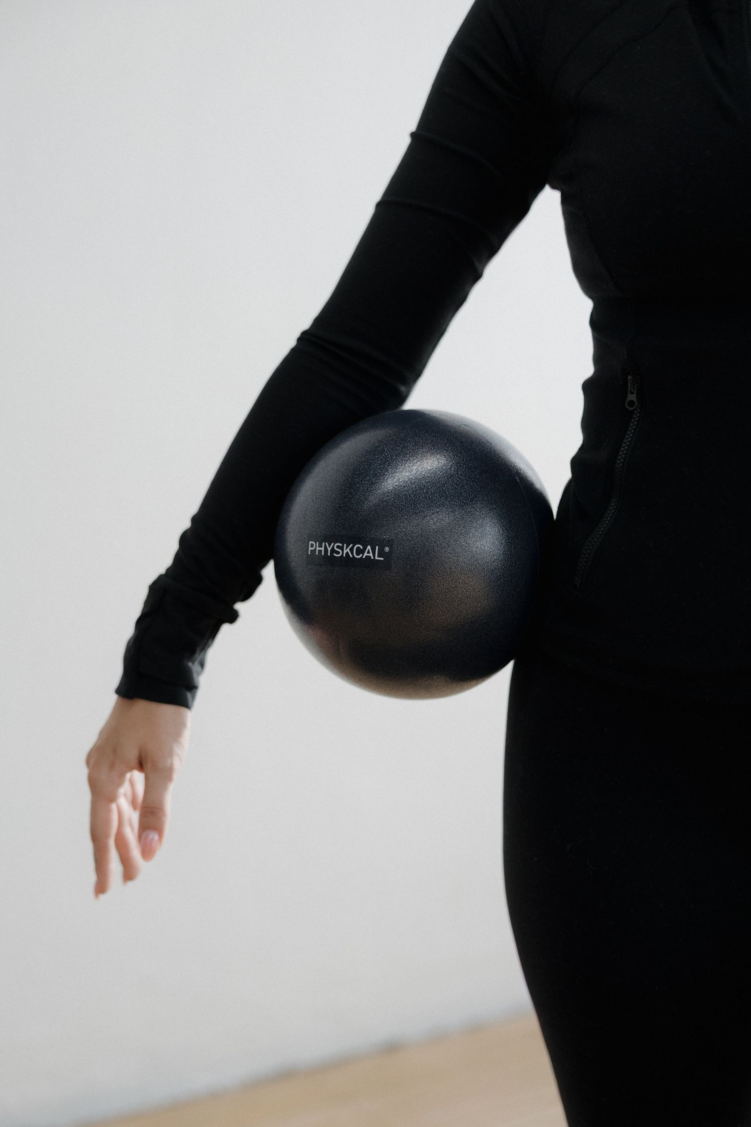 Close-up of woman in black outfit holding a Physkcal brand exercise ball against white background.