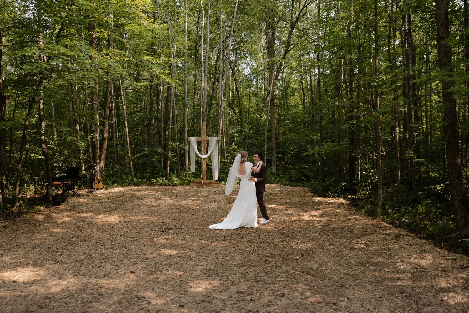 Forest wedding ceremony site with sunlight filtering through trees onto a natural dirt clearing.