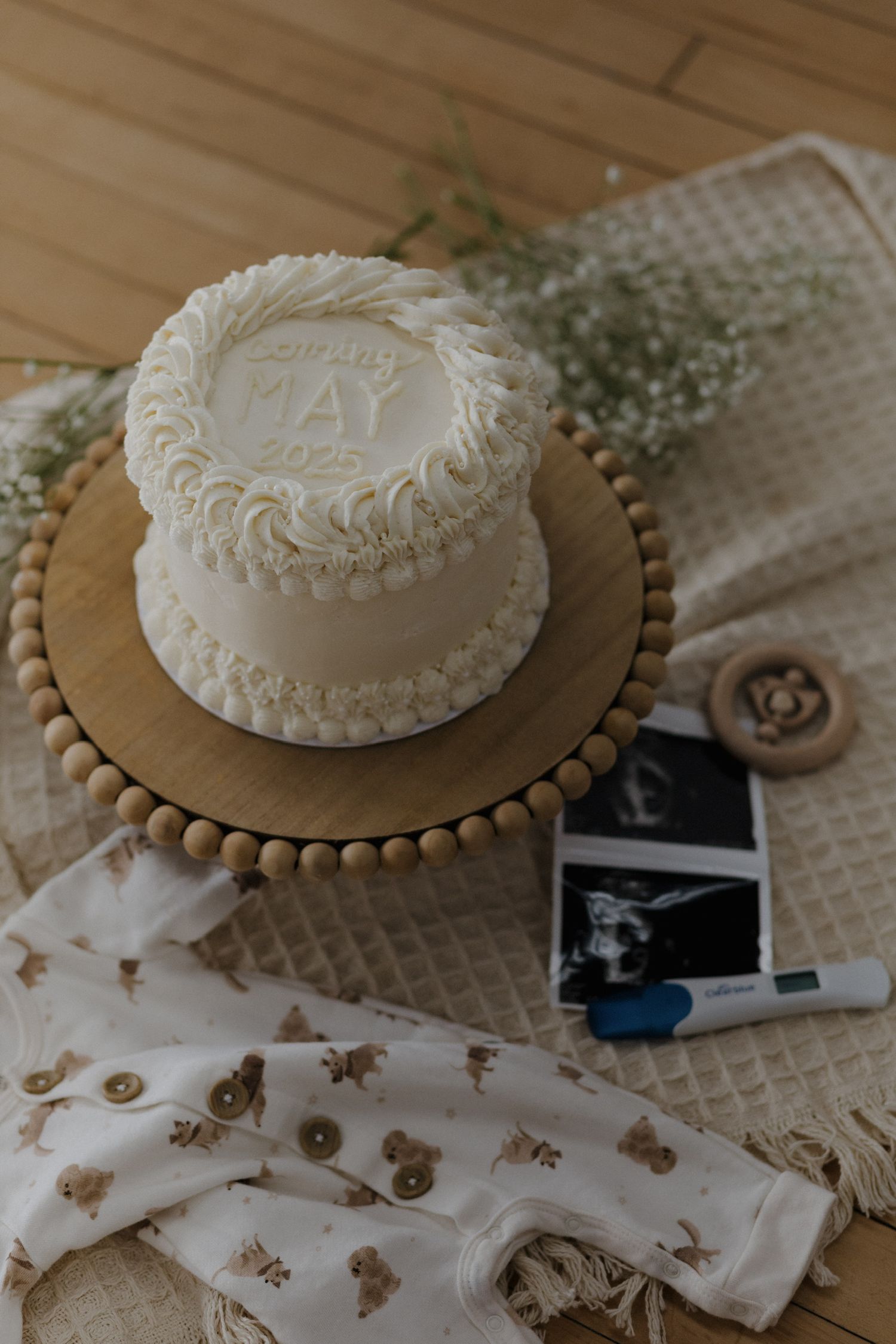 White decorated pregnancy announcement cake with May due date on wooden cake stand with ultrasound photos.
