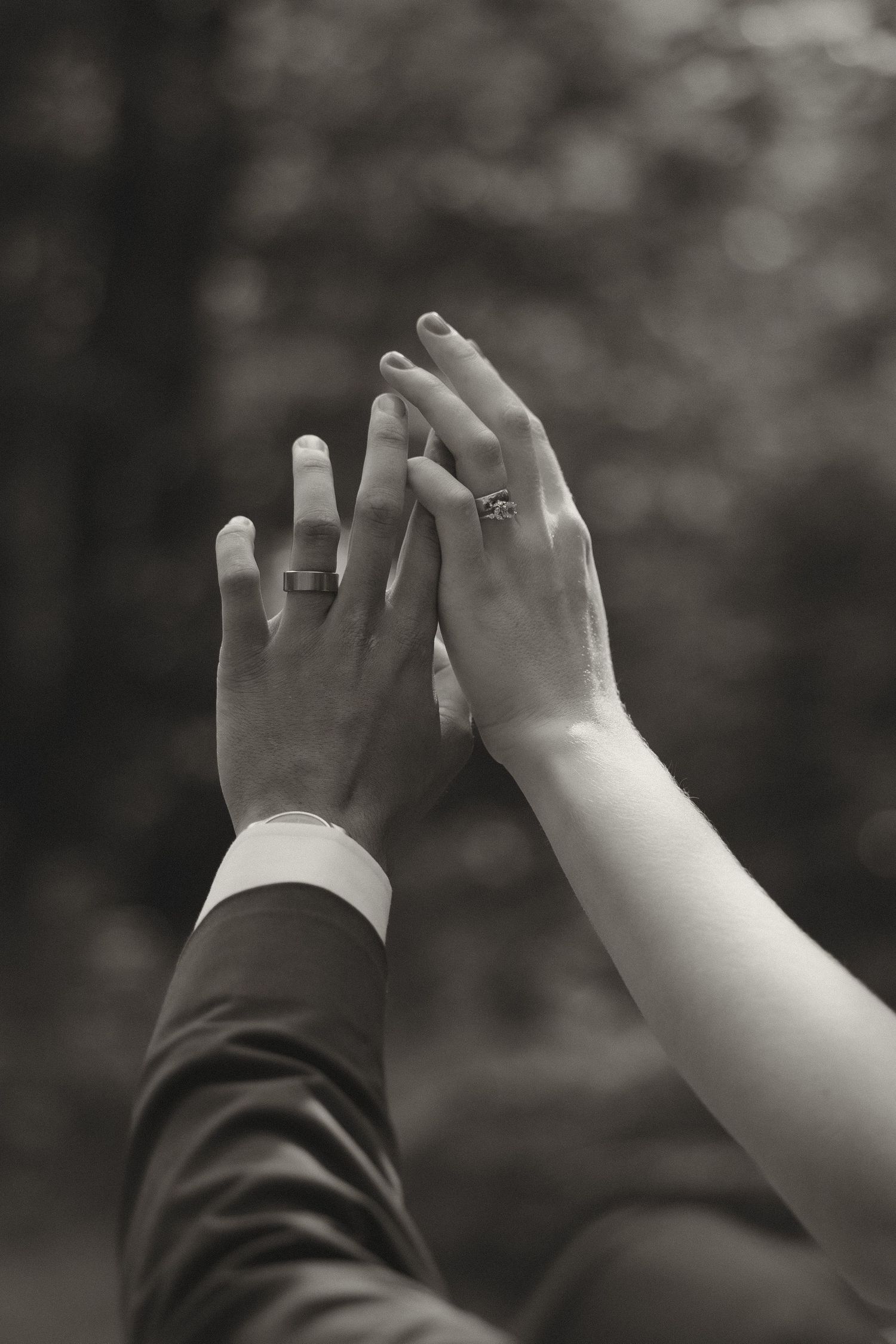 Bride and groom touch hands showing wedding rings in a black and white close-up portrait.